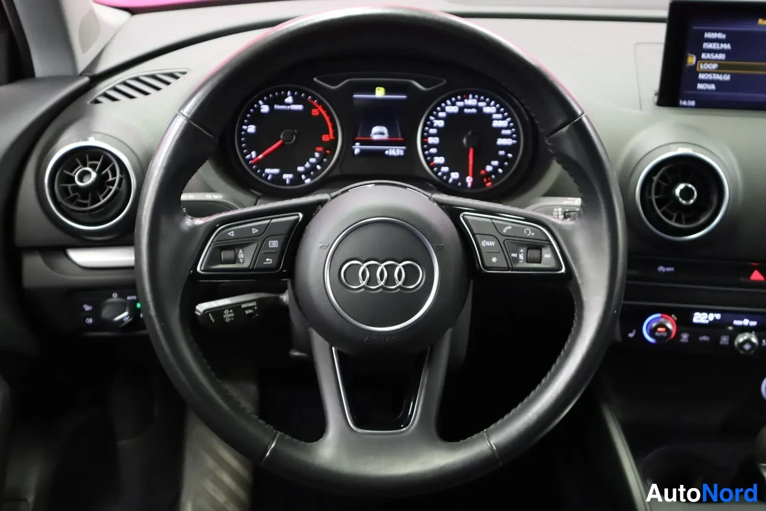 Muu: Audi A3 -henkilöautin ohjaamon näkymä: musta ohjauspyörä, analogiset mittarit ja mmr-näyttö, jossa valikot NAHIN, ASEMA, LOOP, MUSIIKKI, UUTISET.