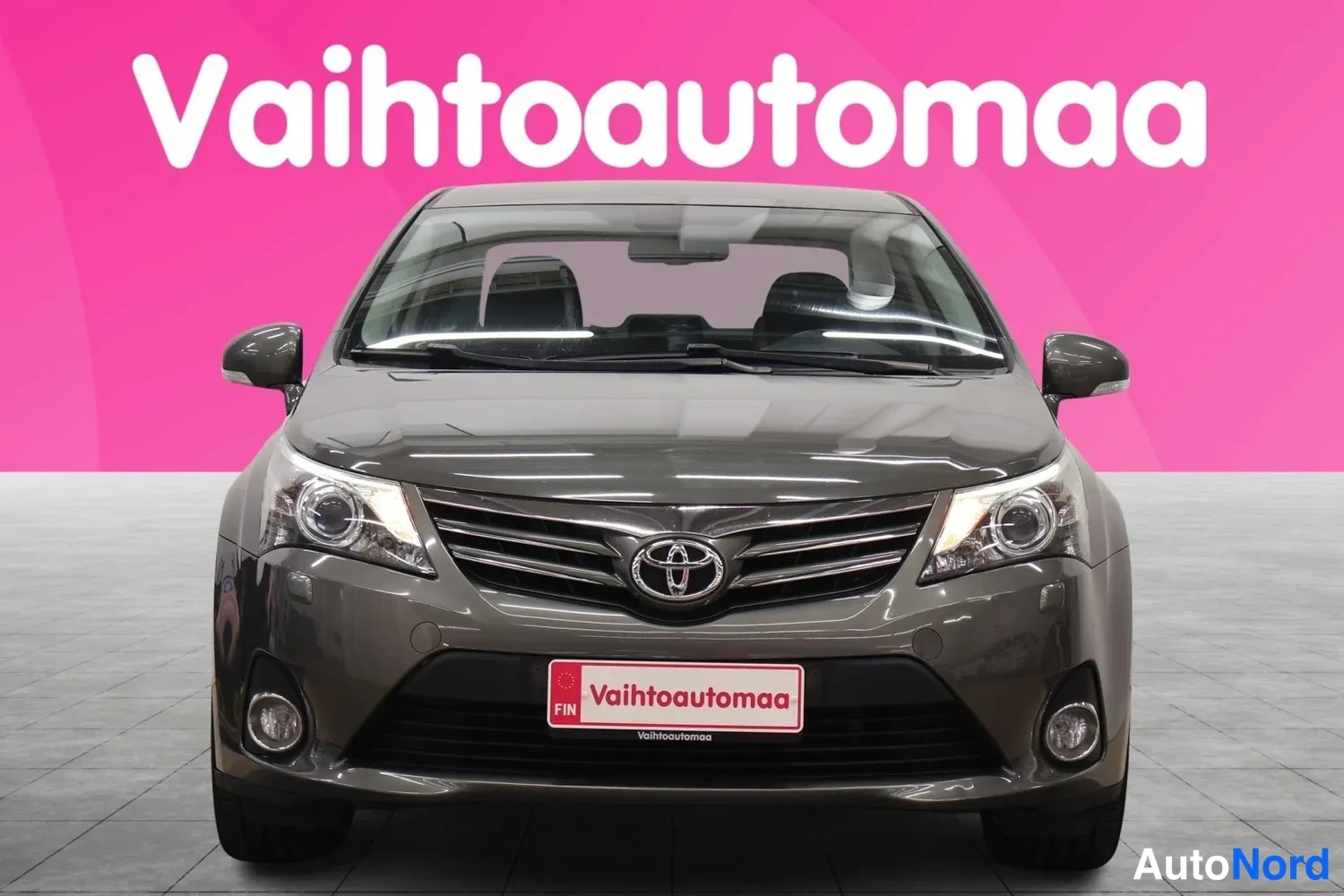 Edestä: Auton etupää suoraan edestä; harmaanruskea sedan, Toyota-merkki grillissä, sumuvalot puskurissa.