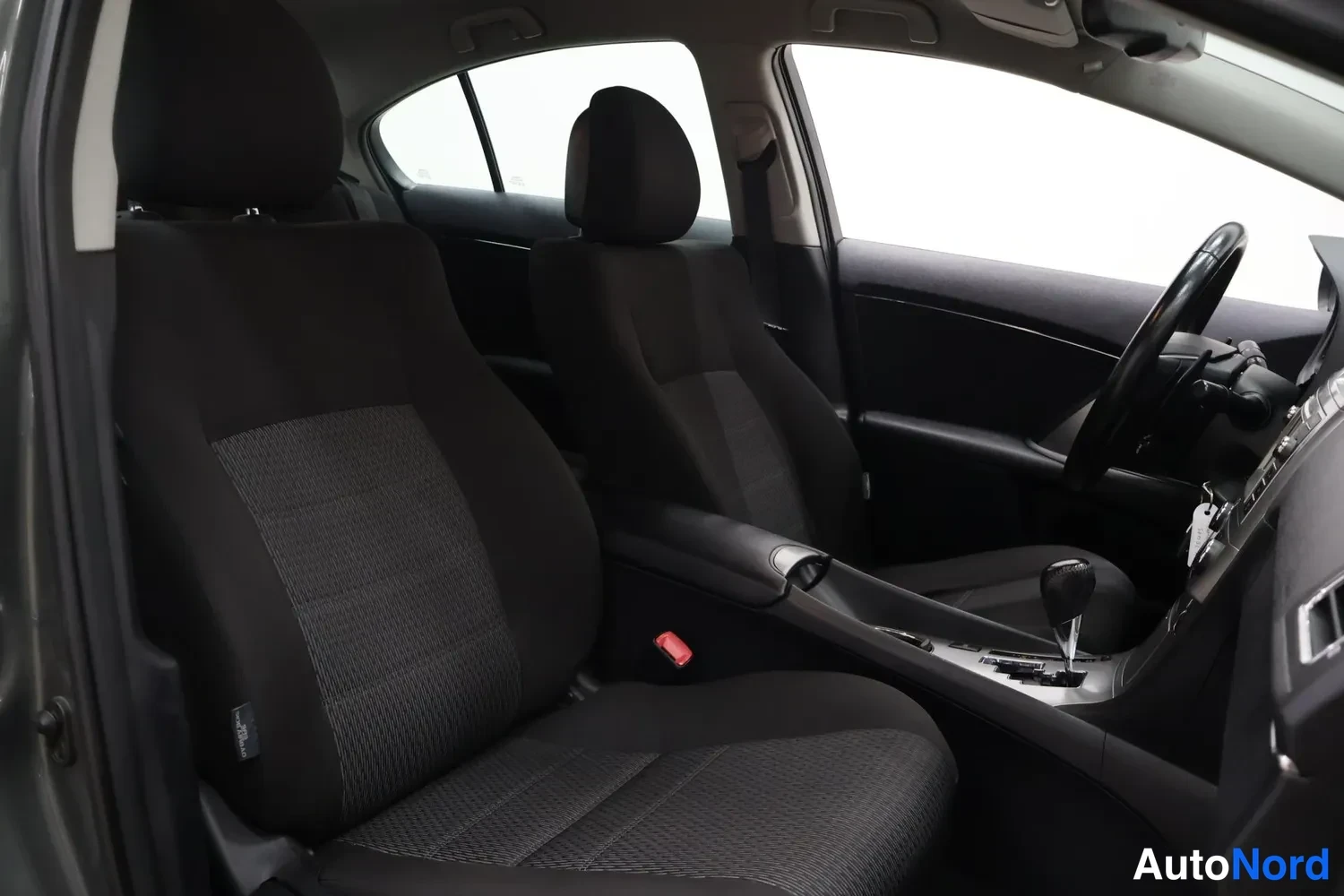 Muu: Autojen sisätilat etumatkustajan puolelta: tummia kankaaksiatuja, keskikonsoli vaihtajan kahvalla ja ohjauspyörä oikealla.