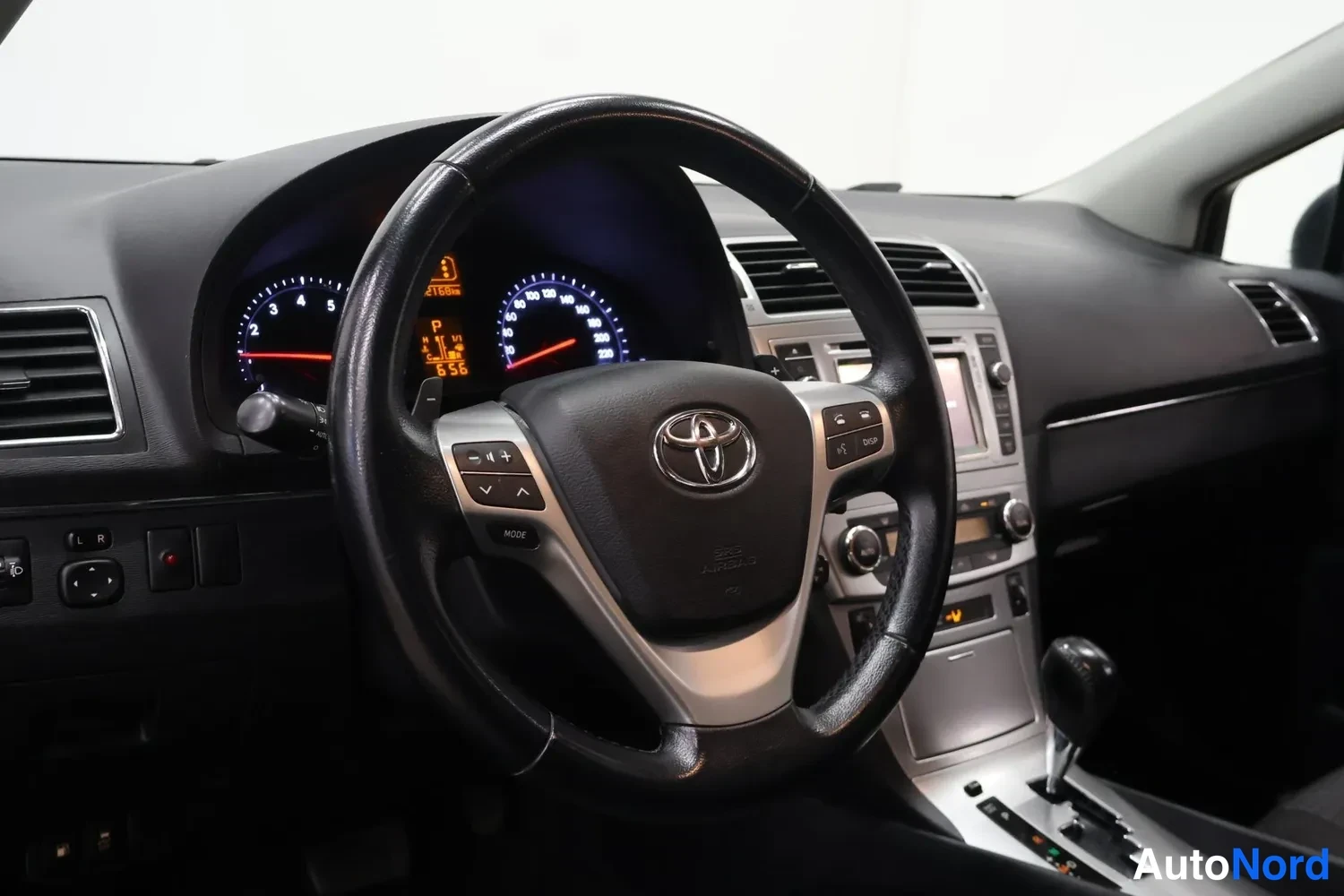 Muu: Ajonäkymä kuljettajan paikalta: ohjauspyörä Toyota-logolla, mittaristo taustavalossa, radio- ja keskusyksikkö, vaihteenvalitsin.