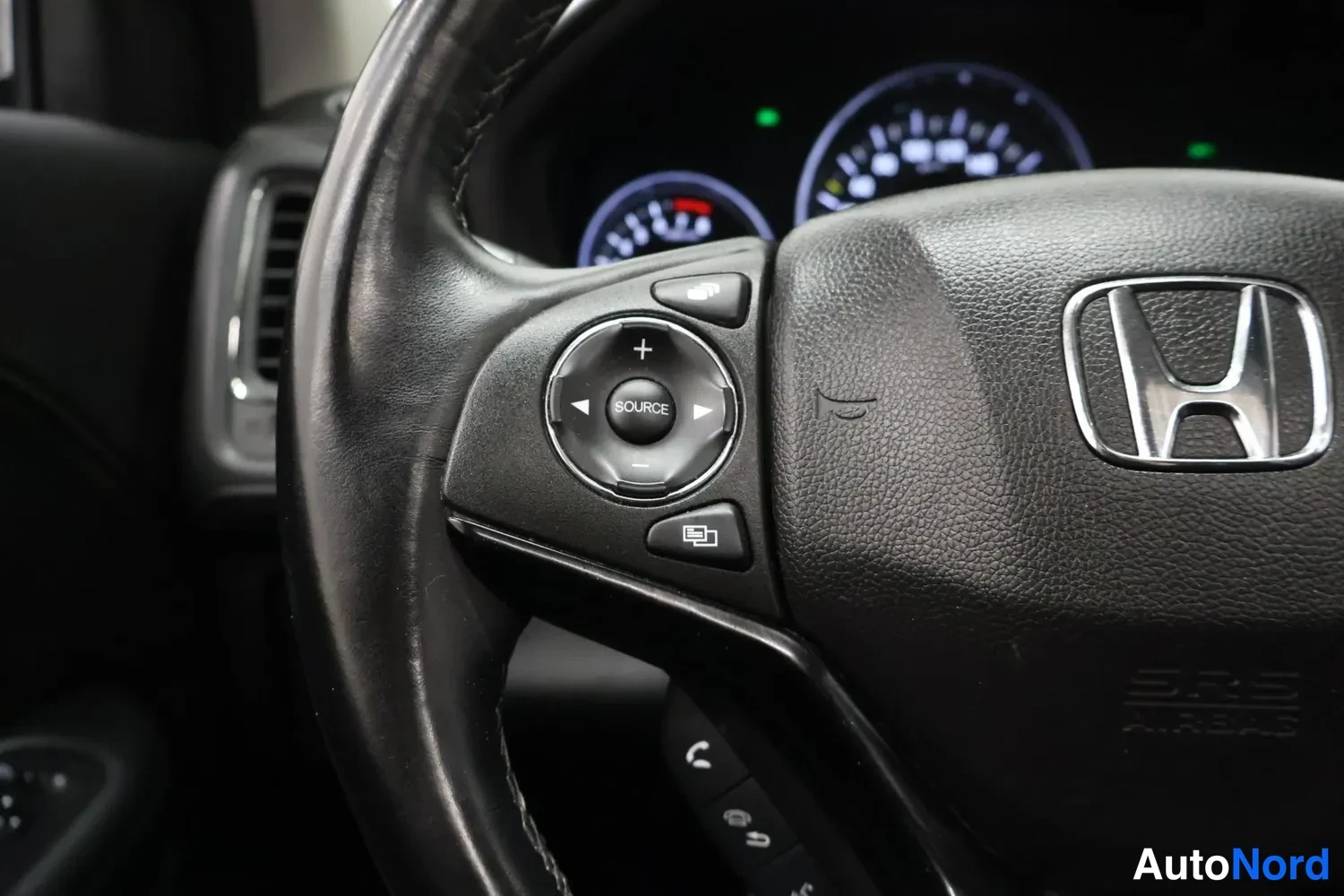 Yksityiskohta: Ohjauspyörän vasen puoli: Honda-logo, SOURCE- ja äänenvoimakkuuspainikkeet, taustalla osittain näkyvät mittarit.