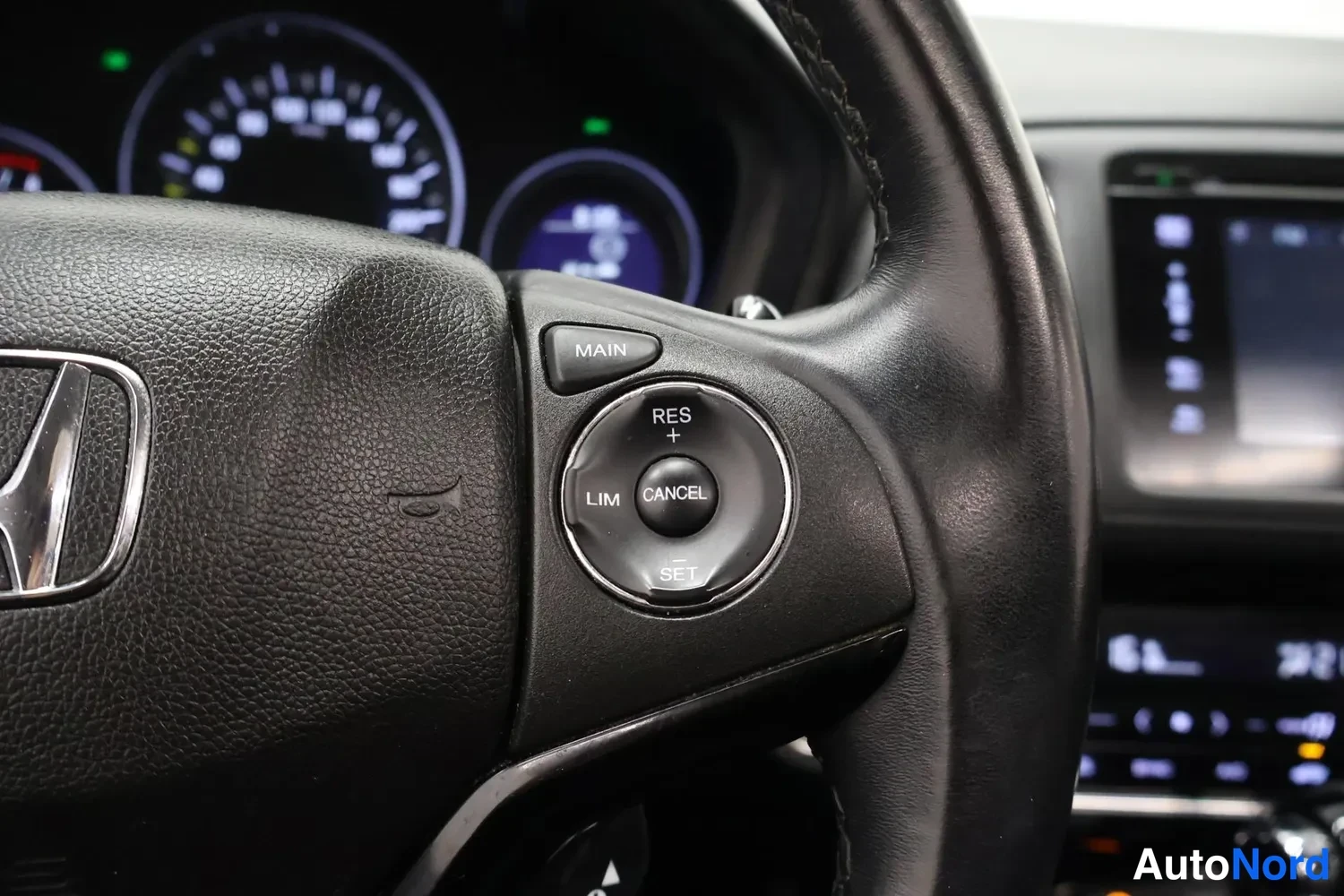 Yksityiskohta: Ohjauspyörän oikea puoli: Honda-logo, risteilytelineen painikkeet MAIN, RES, CANCEL, LIM ja SET, taustalla kojelauta ja näyttö.