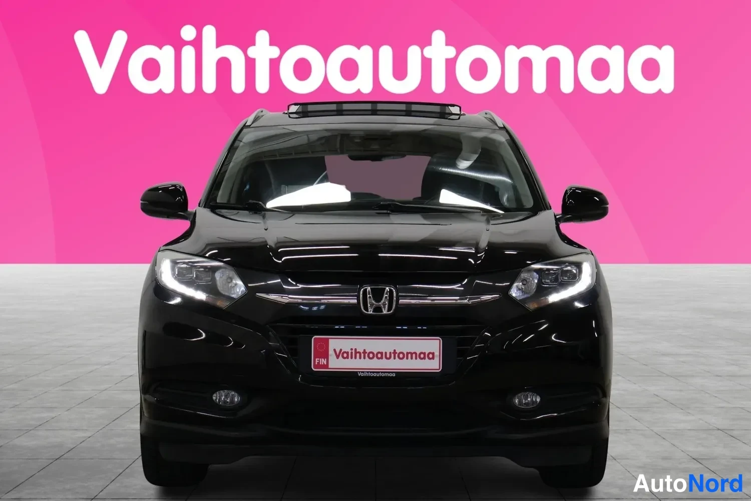 Edestä: Mustan Honda HR-V:n suora etukuva, etusäleikkö, kilpi ja ajovalot näkyvät pinkillä taustalla.