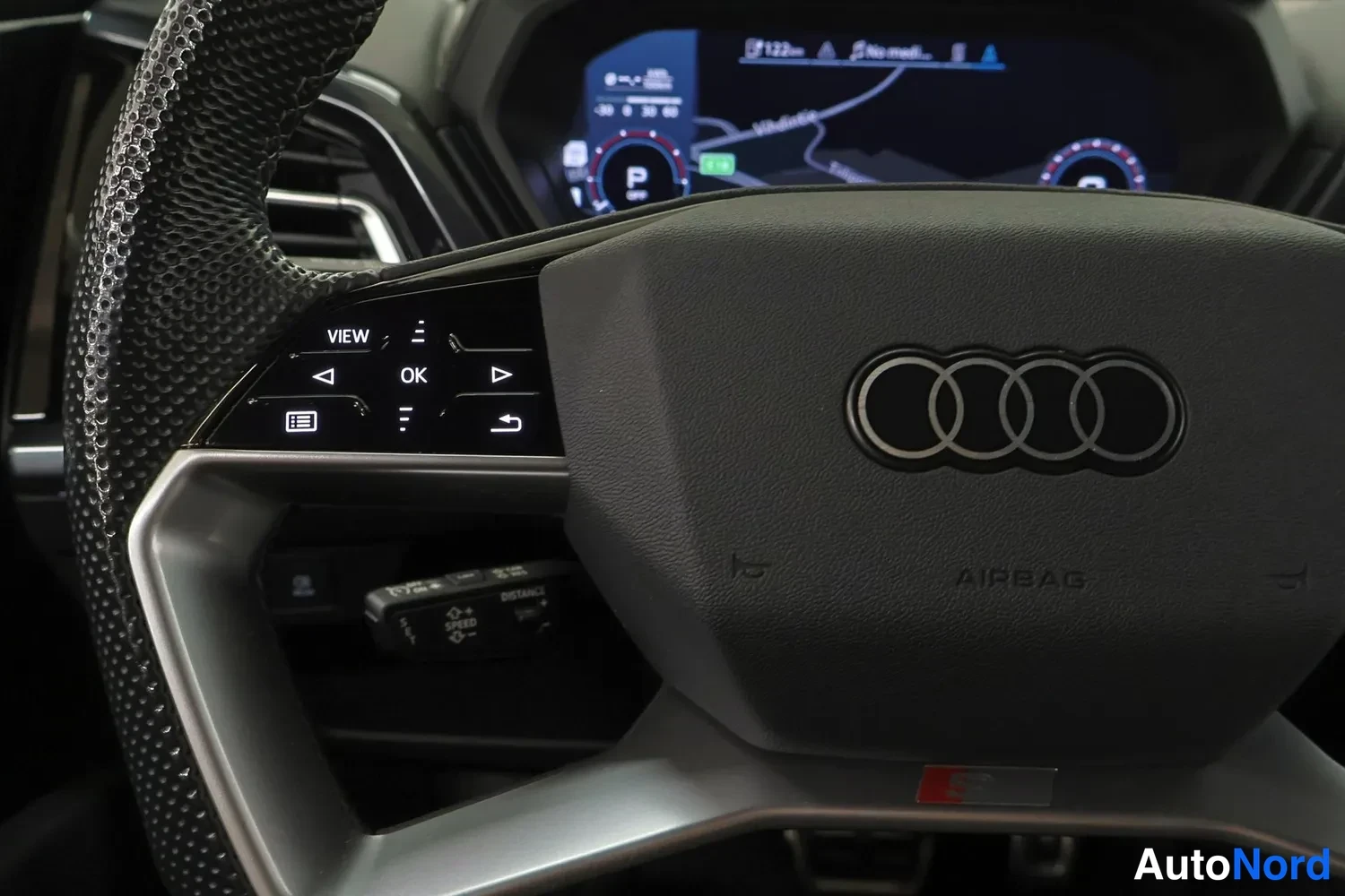 Muu: Lähikuva Audin ohjauspyörästä: AIRBAG-teksti, Audi-korumerkki ja vasemman puolen monitoimpainikkeet (VIEW, OK).