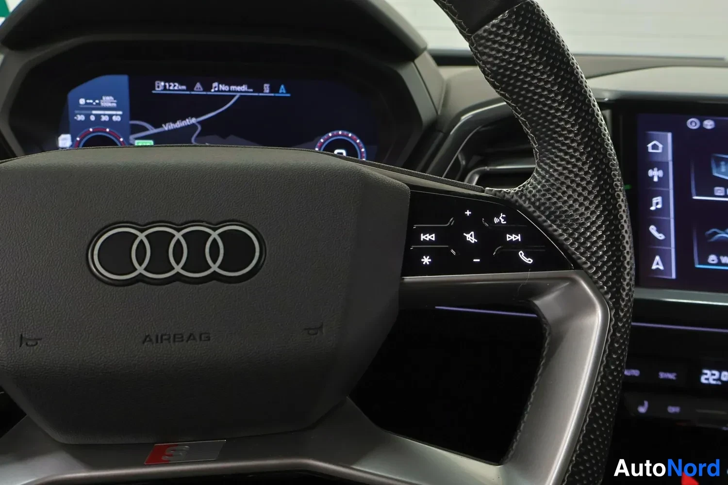 Muu: Audi-ohjauspyörä, jonka keskiössä neljä renkaan logoa ja AIRBAG-teksti, taustalla mittaristö ja keskikonsolin näyttö.