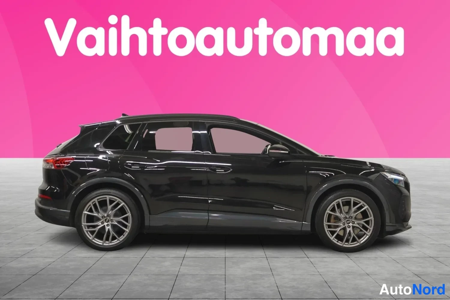 Etuviisto, nokka oikealle: Mustan Audi Q4 e-tronin sivukuva, vasen kylki ja keulan etureuna näkyvissä pinkillä taustalla.