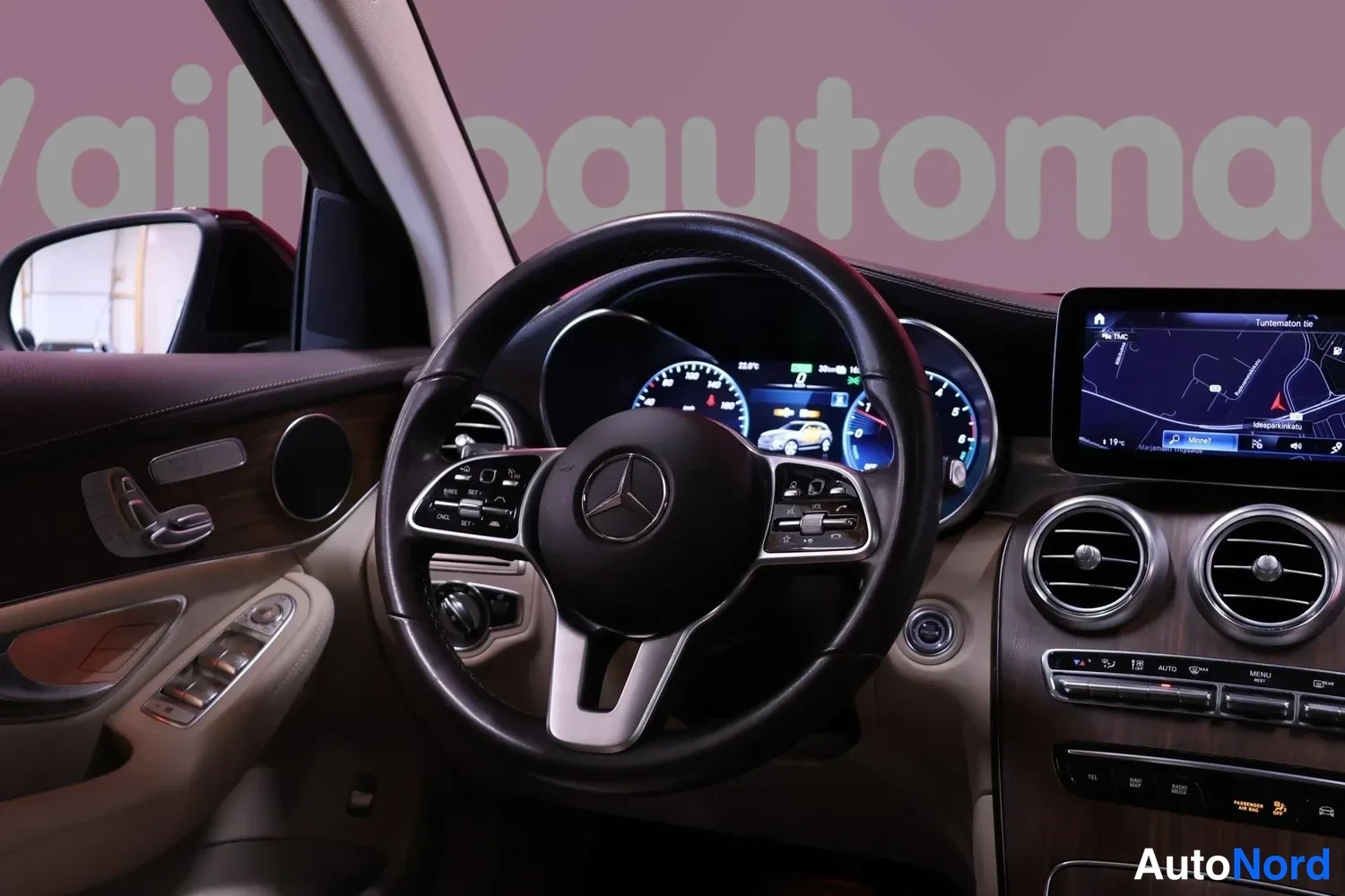 Yksityiskohta: Ohjaamon näkymä kuljettajan puolelta: Mercedes-merkkinen ohjauspyörä, näyttömittaristo, keskinäyttö navigointikartalla ja ovipaneeli säädinpainikkeineen.