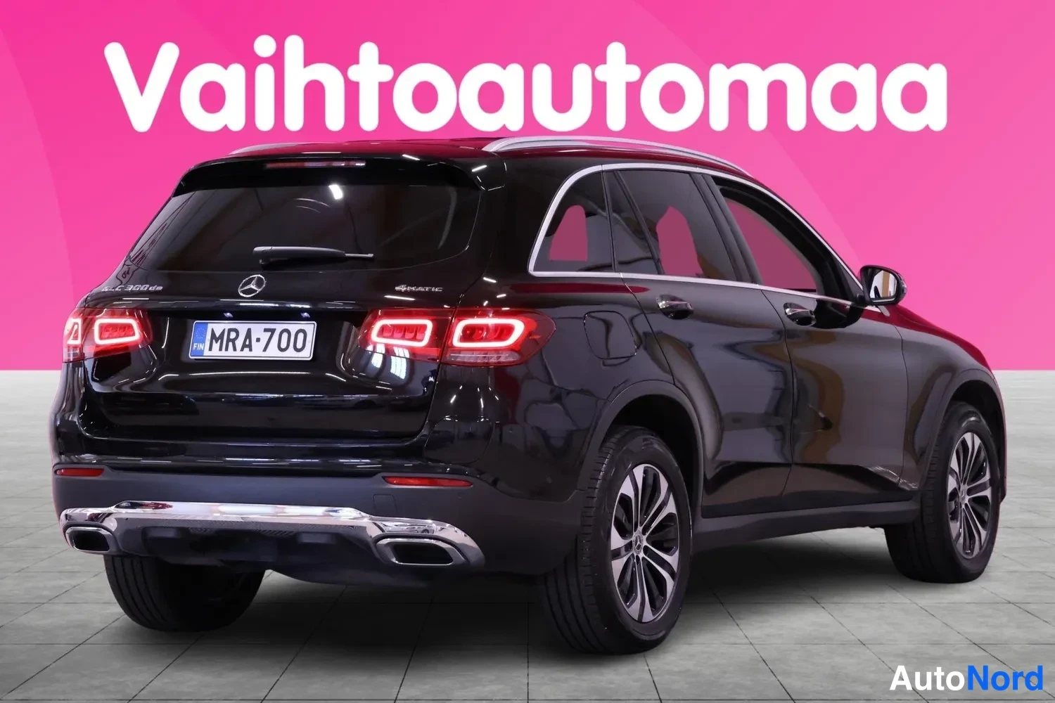 Takaviisto: Rear three-quarter view of a black SUV showing the left flank and rear face against a pink background with white text 'Vaihtoautoma'. The red tail lights, chrom