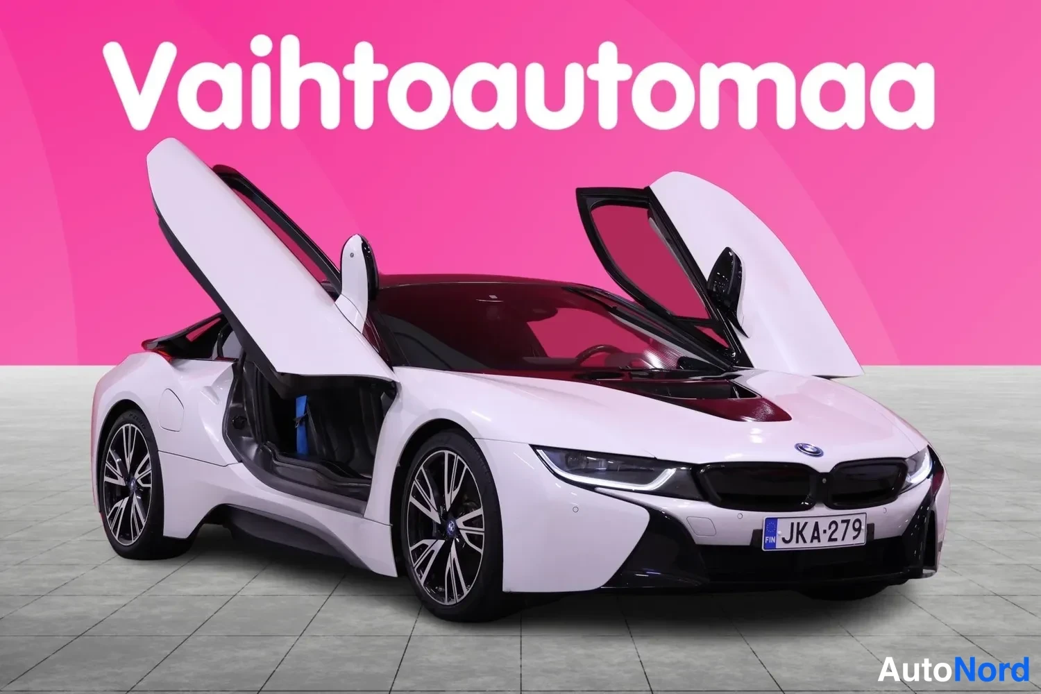 Etuviisto, nokka oikealle: Valkoinen BMW i8Avautuvilla ovilla ylhäällä, etusäleikkö ja kylki näkyvät, rekisteritunnus.