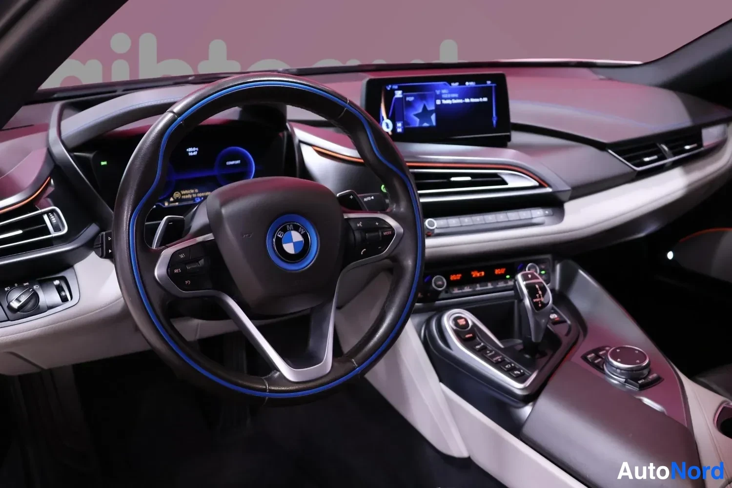 Muu: BMW i8:n sisätilat: ohjauspyörä sinisellä reunuksella, keskellä kosketusnäyttö ja vaihteenvalitsin, tumma ja vaalea kojelauta.
