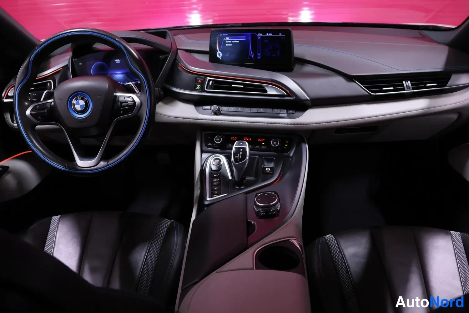 Muu: BMW i8:n kojelauta edestä: ohjauspyörä sinisin reunoineen, infotainment-näyttö ylhäällä ja keskikonsolin vaihteenvalitsin.