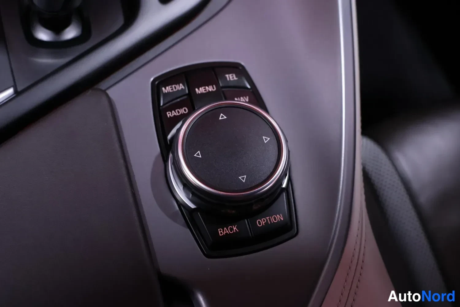 Yksityiskohta: Sisätilakuvan lähikuva: iDrive-ohjainkiekko ja sen ympärillä MEDIA-, MENU-, TEL-, NAV-, RADIO-, BACK- ja OPTION-napit.