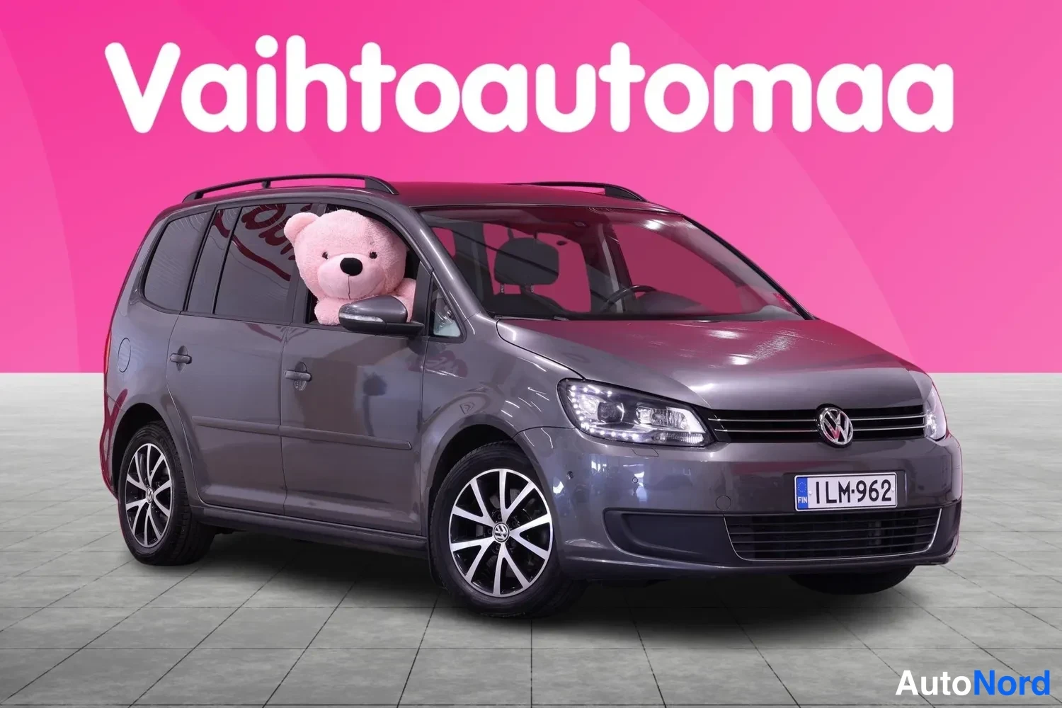 Etuviisto, nokka oikealle: Tummanharmaa Volkswagen Touran -tila-auto kuvattuna etuviistosta oikealta; rekisteritunnus, kattokaiteet ja kevytmetallivanteet.