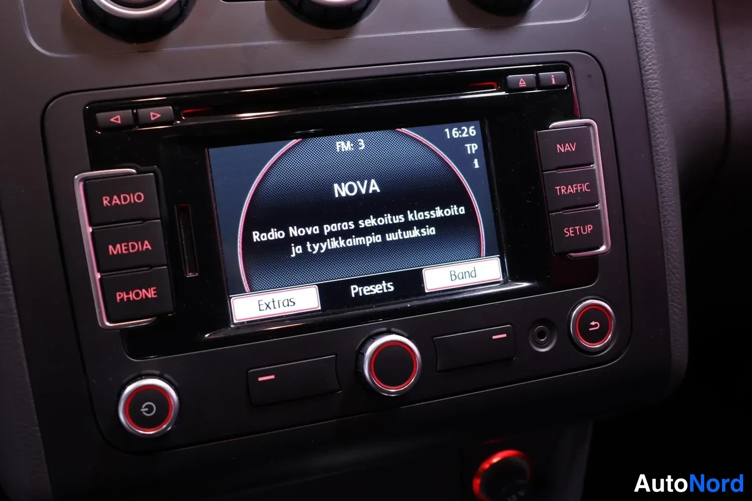 Muu: Kojelaudan radiopaneeli, näytöllä Radio Nova kanavalla FM 3 kello 16:26, sivuilla RADIO-, MEDIA-, PHONE-, NAV-, TRAFFIC- ja SETUP-painikkeet.