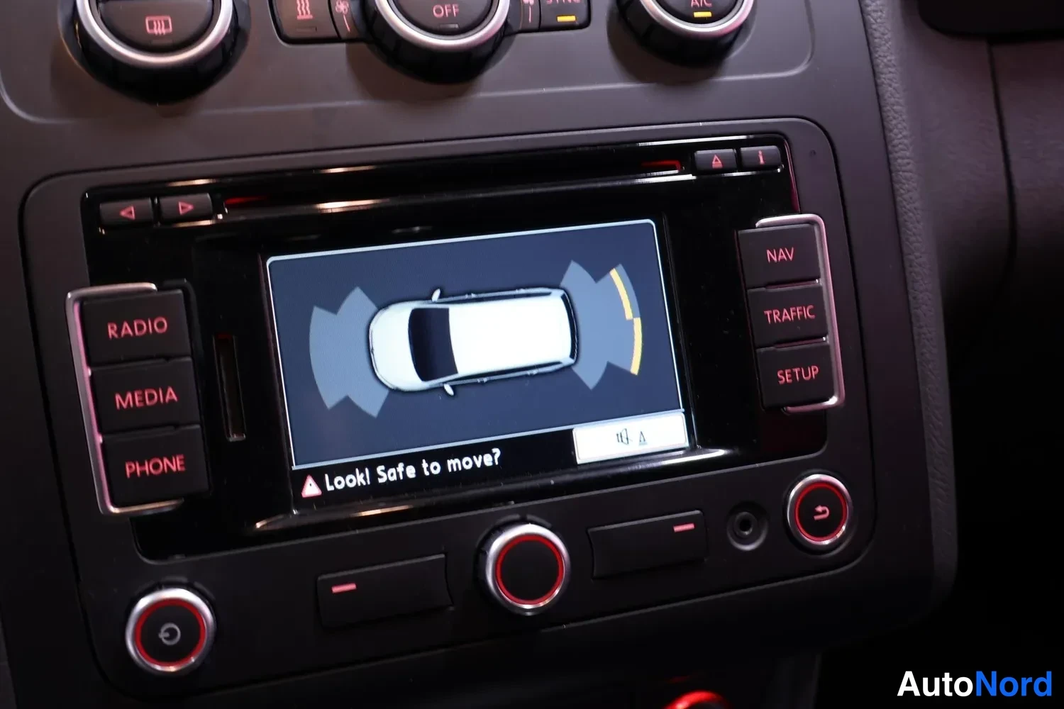 Yksityiskohta: Kojeistossa radiopaneeli, jonka näytössä pysäköintitutkan kuvanto ja teksti 'Look! Safe to move?'. Napit: RADIO, MEDIA, PHONE, NAV, TRAFFIC, SETUP.
