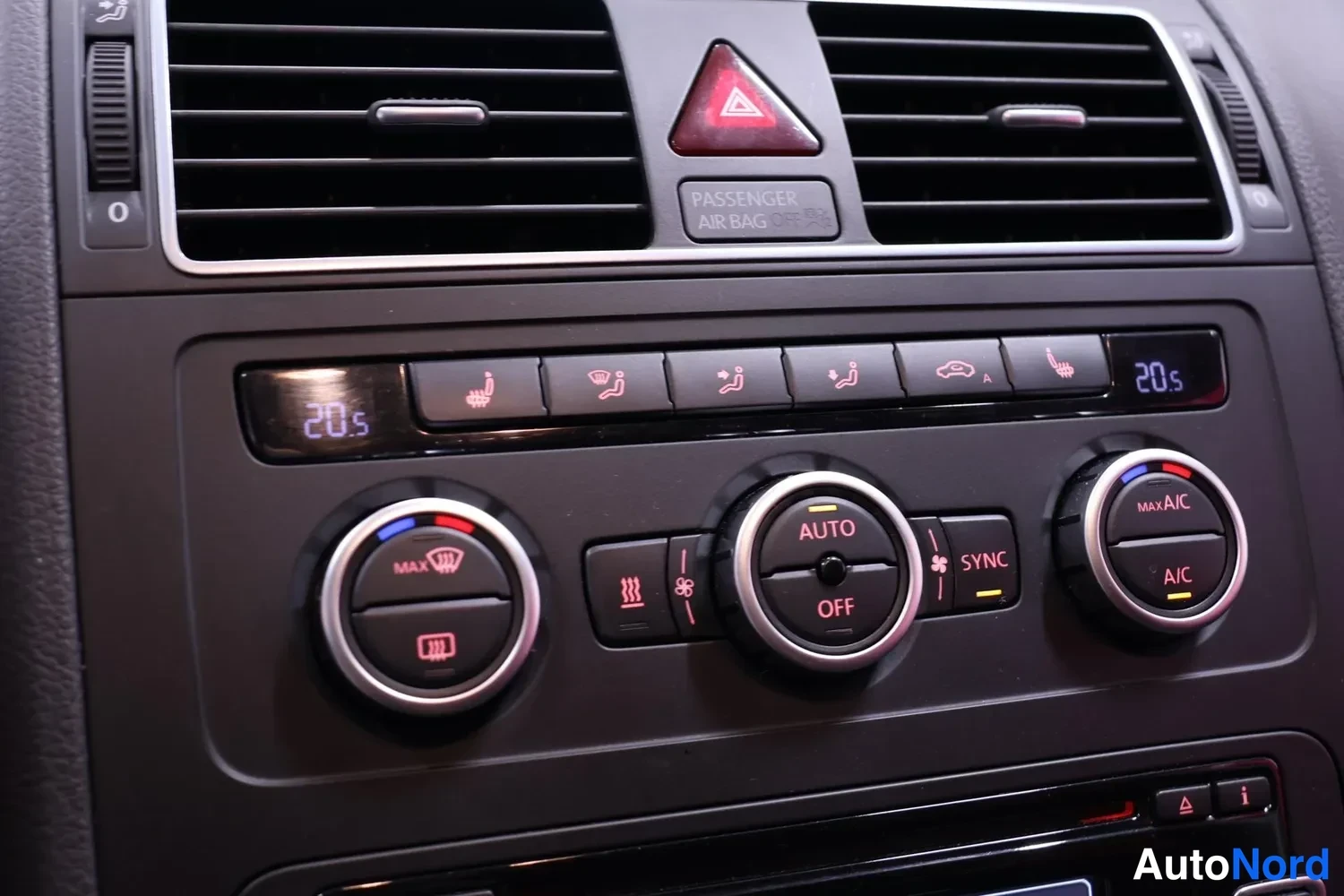 Yksityiskohta: Keskiö instrumentit: lämpötilat näyttävät 20,5 °C, säätönupit AUTO/OFF, SYNC, A/C ja MAX A/C, ylhäällä varoitus painonappi ja teksti 'PASSENGER AIR BAG OFF'.