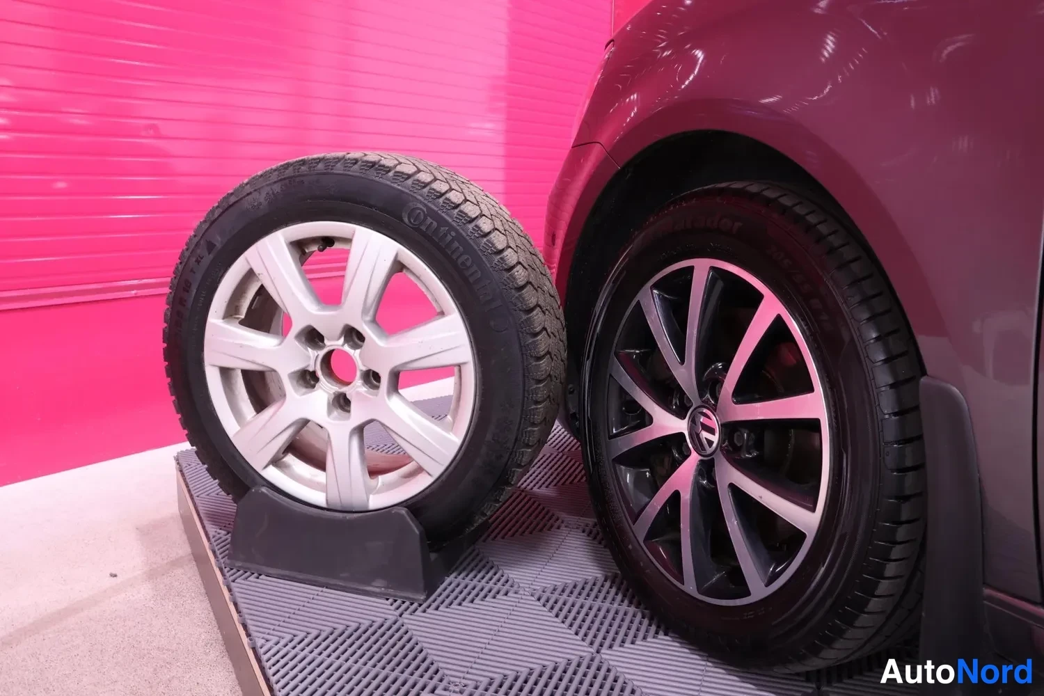Yksityiskohta: Varapyörä hopeaisella vanteella ja nalikkuvanteisella talvirenkaalla pystyssä auton mustaa kevytmetallivannetta ja Volkswagen-merkkiä vasten.
