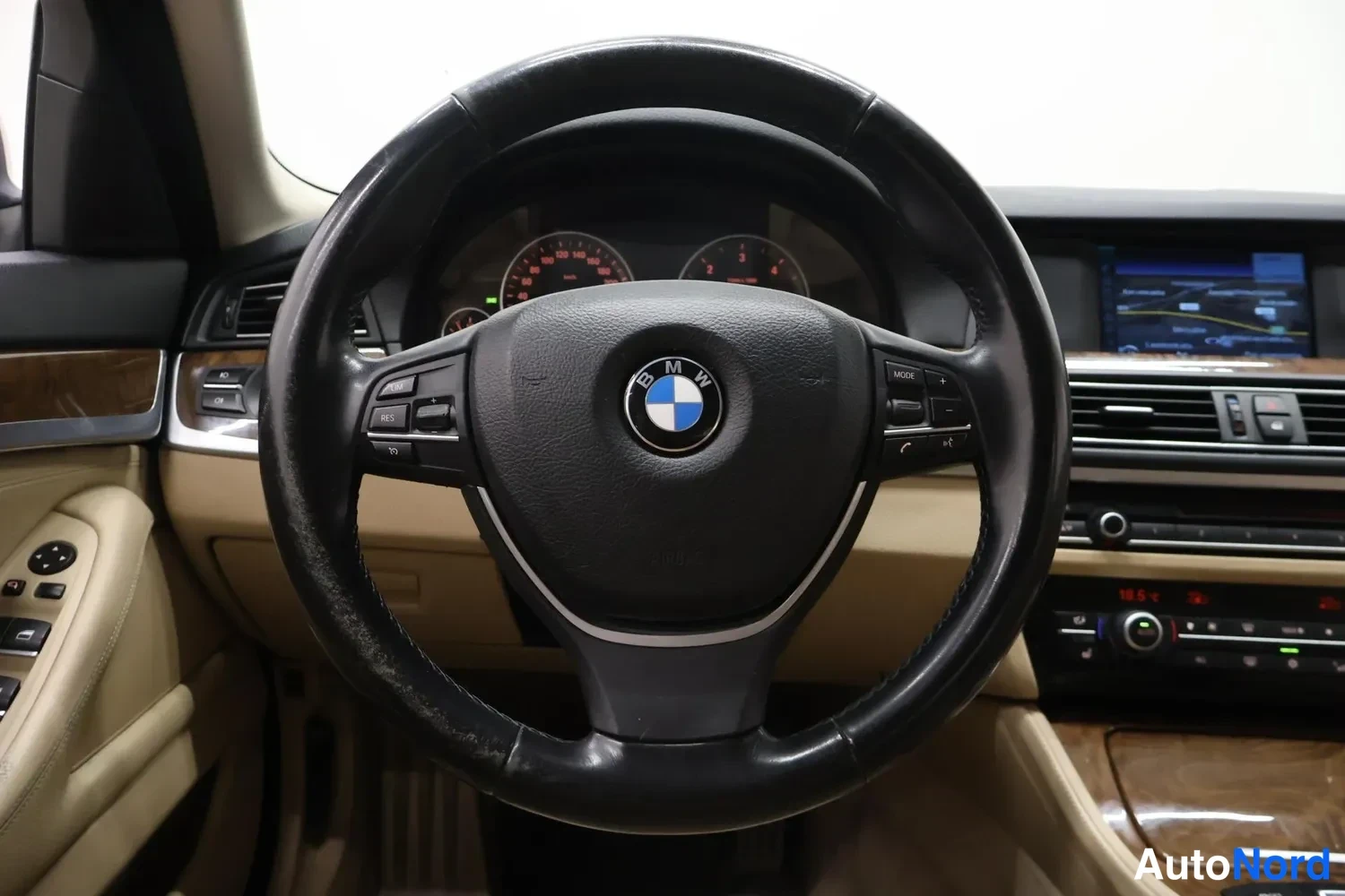 Yksityiskohta: Ohjauspyörän lähikuva BMW-logolla, taustalla mittaristo, näyttö ja kojelaudan säätimet.