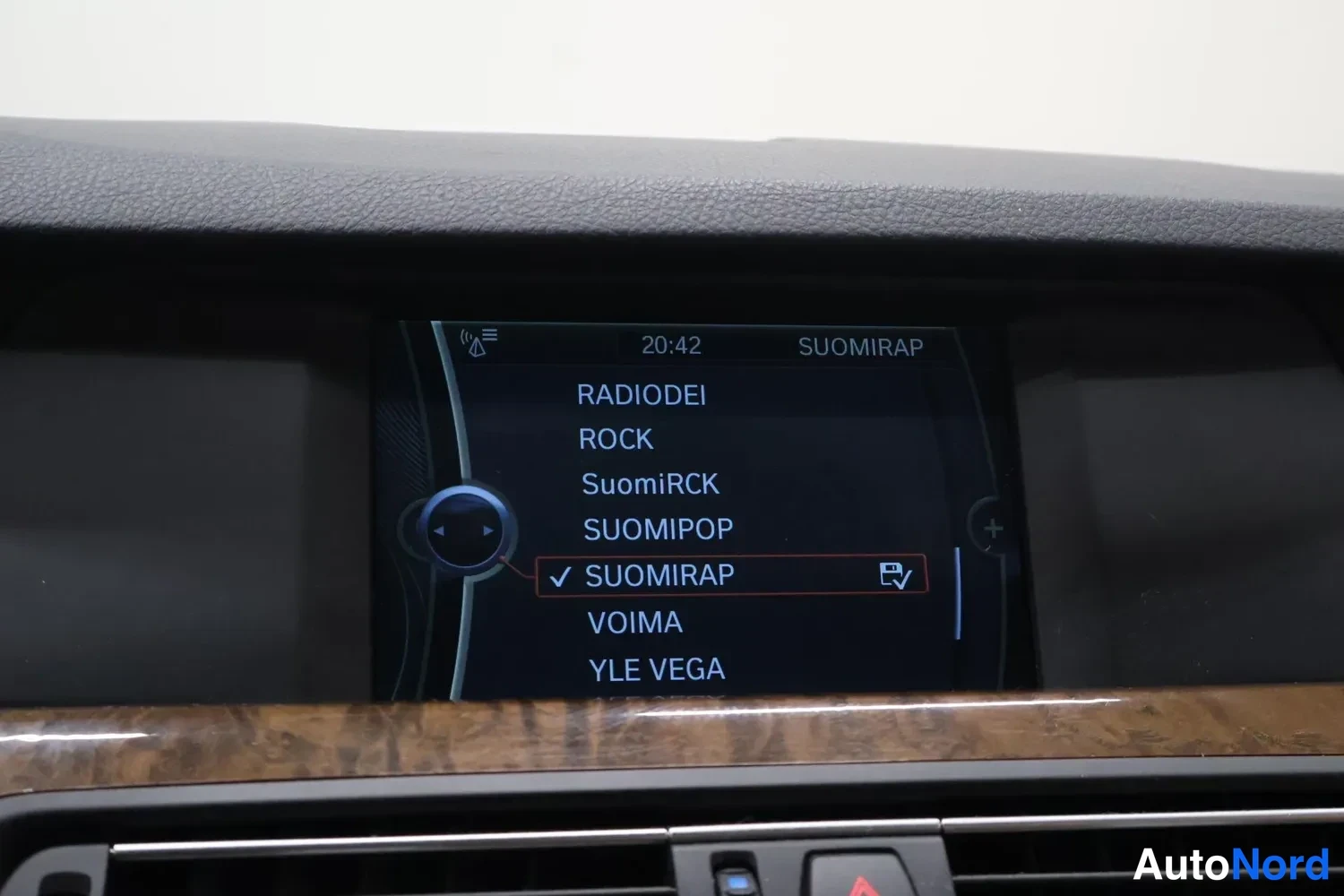 Yksityiskohta: Auton kojelaudan infotainment-näyttö lähikuva. Näytössä radiokanavaluettelo: RADIODEI, ROCK, SuomiRCK, SUOMIPOP, SUOMIRAP (valittu rastilla), VOIMA ja YLE VEGA.