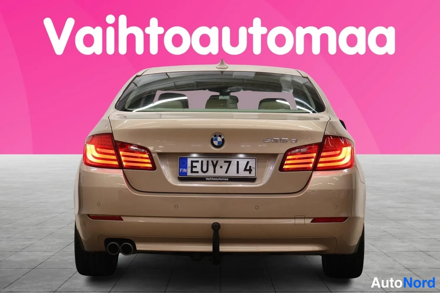Takaa: Beige sedan suoraan takaa, rekisteritunnus, takavalot päällä.