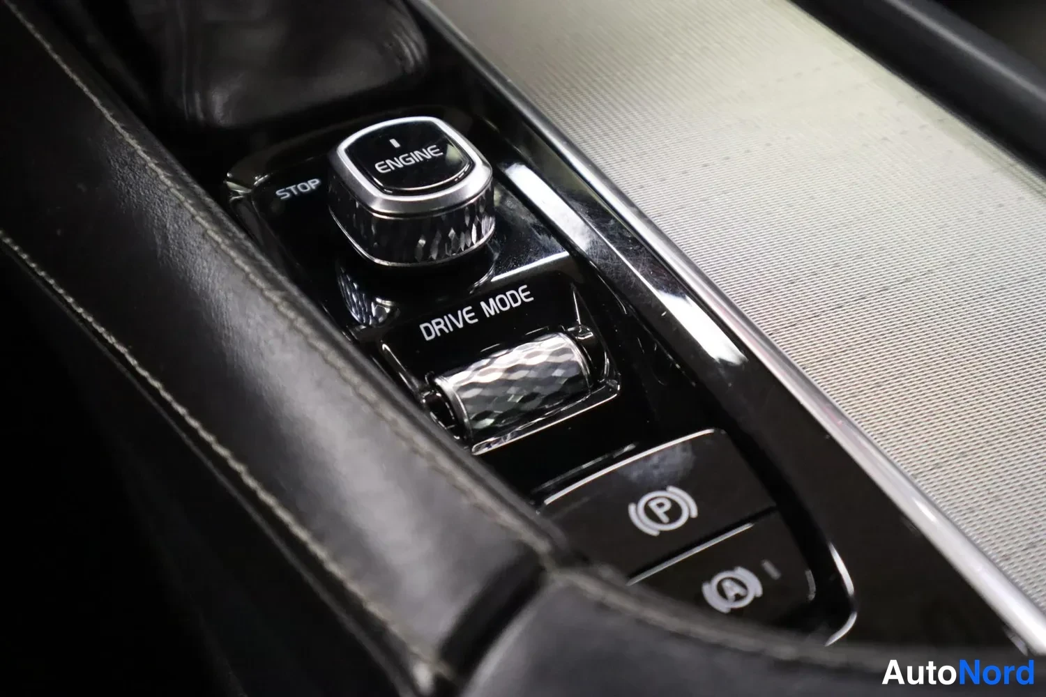 Yksityiskohta: Keskikonsolin käynnistysnuppi, jossa tekstit START/STOP ENGINE ja DRIVE MODE -valitsinrulla, sekä sähköinen parkkirngun jarrunappi ja auto hold -toiminnon nappi