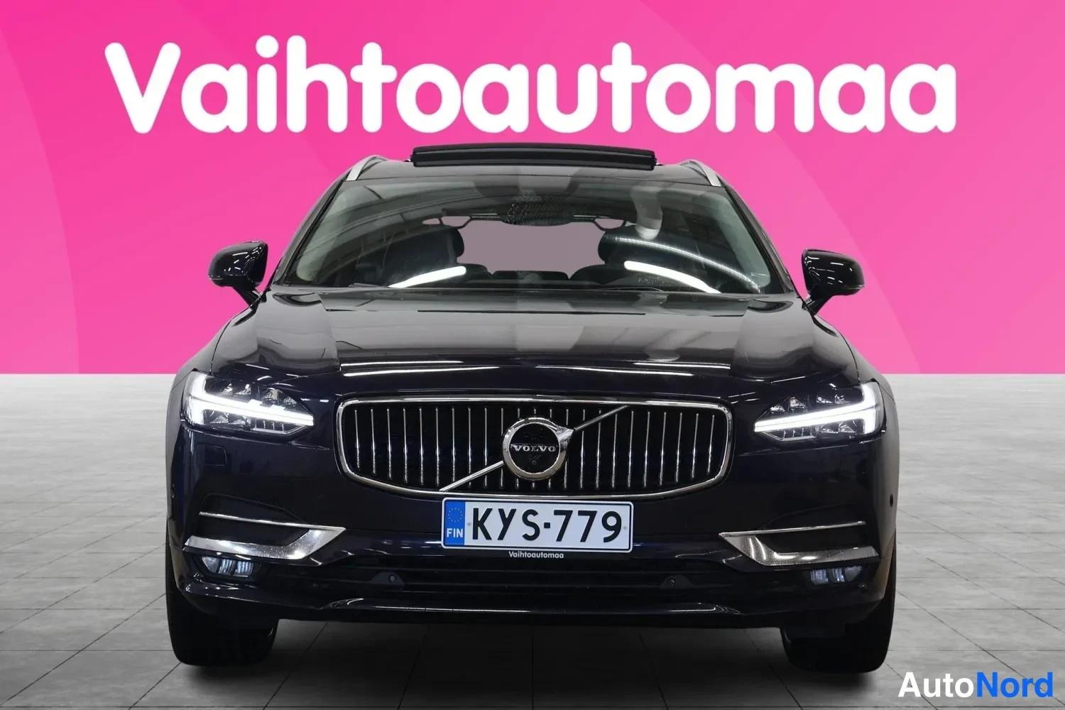 Edestä: Tummansinisen Volvo V90:n etunäkymä suoraan edestä, panoraamakatto auki, rekisterikilpi.