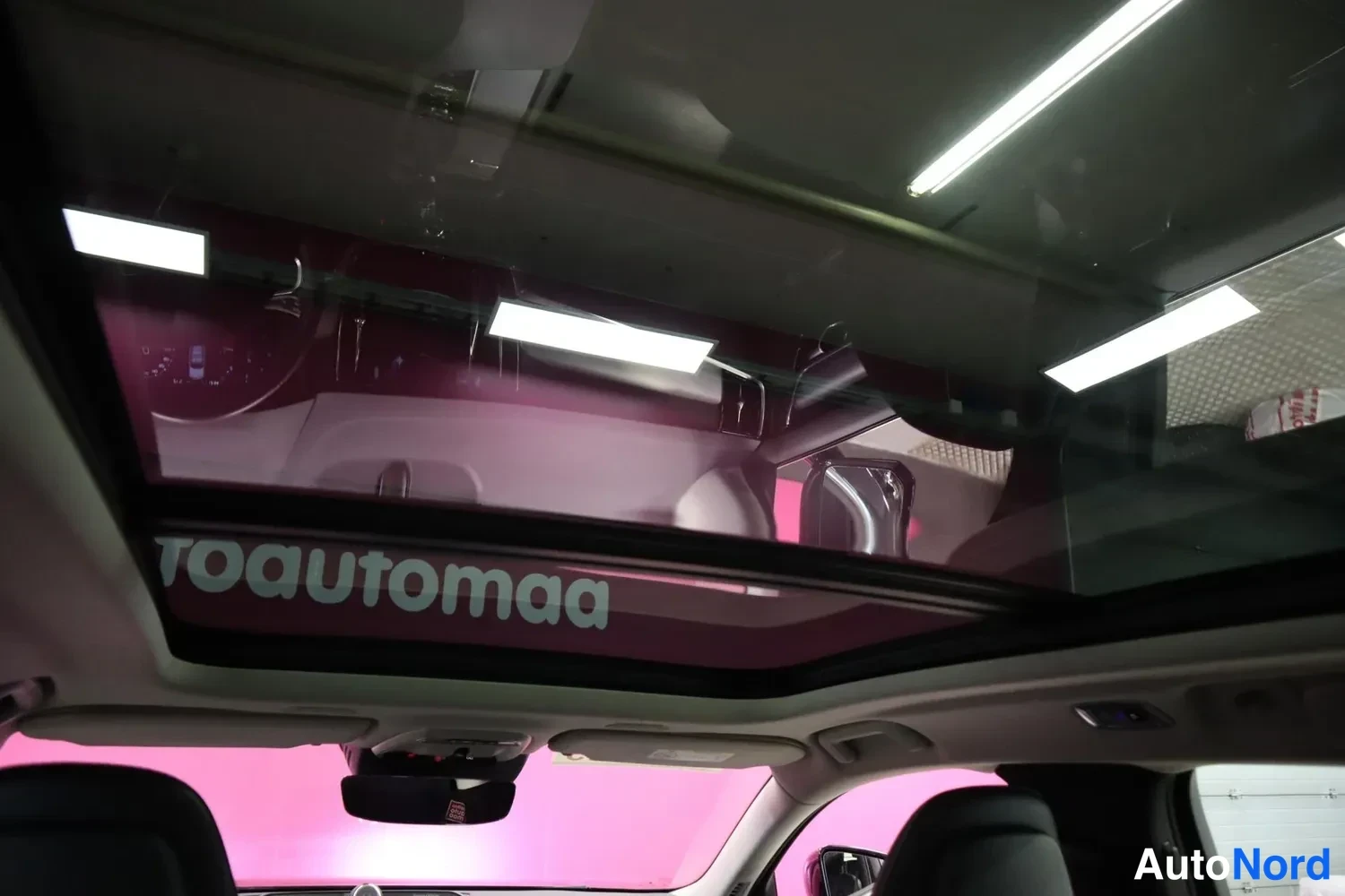 Muu: Panoraamikattoikkuna auton sisältä kuvattuna, lasin pinnassa heijastuu pinkki tausta ja teksti toautomaa.