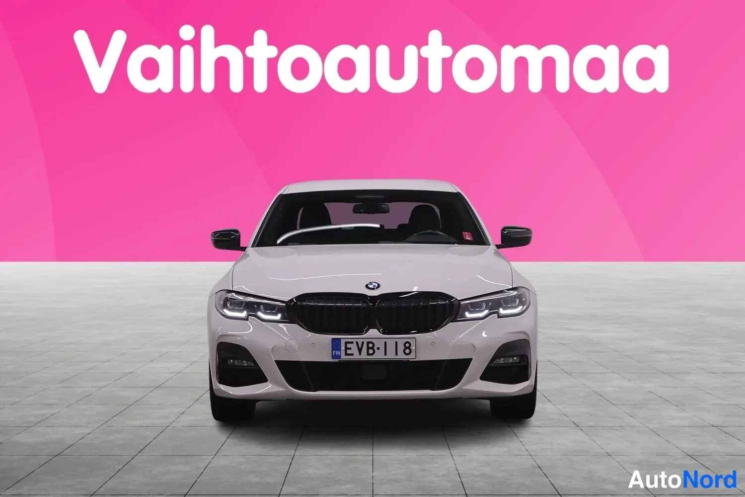 Edestä: BMW henkilöauto suoraan edestä, valkoinen kori, musta etusäleikkö, EV-tyyppiset etuvalot ja rekisteritunnus.