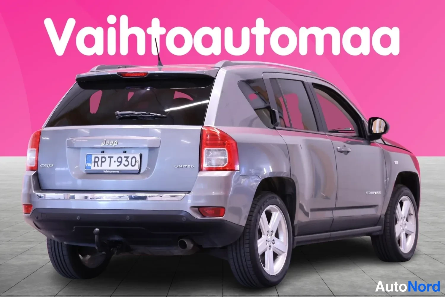Takaviisto: Rear three-quarter view of the silver Jeep Compass Limited with rear tail lights, boot lid, towing hitch and chrome trim. The driver’s side flank is also visibl