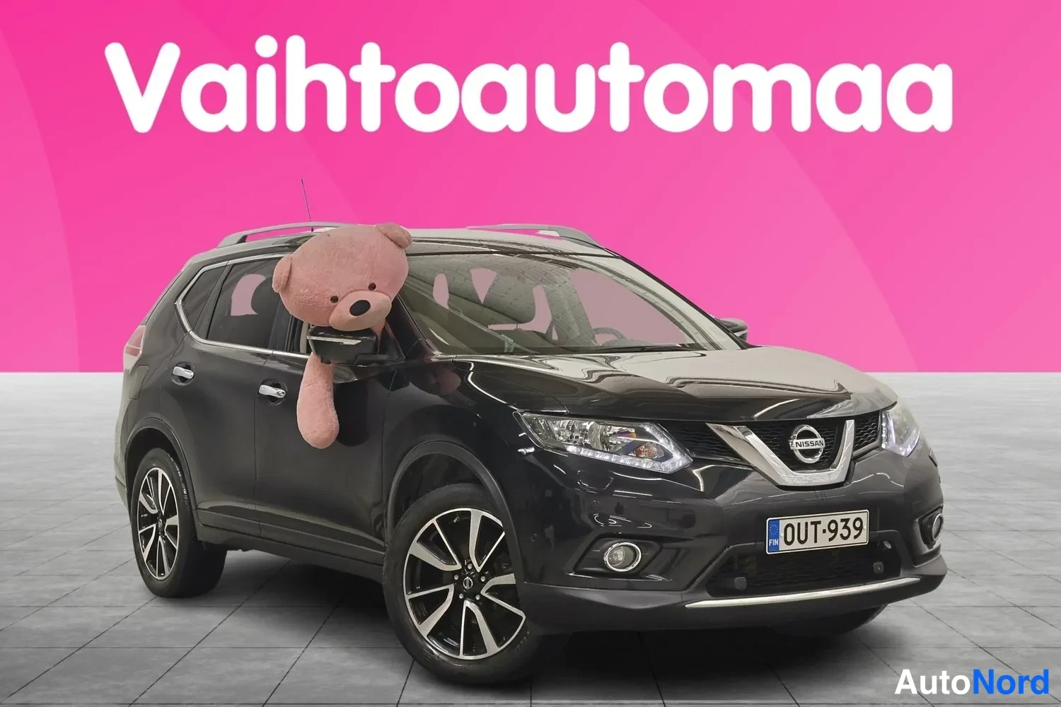 Etuviisto, nokka oikealle: Musta tila-auto vinosta edestä oikealta kuvattuna, rekisterikilpi, peilistä roikkuu pehmolelu.
