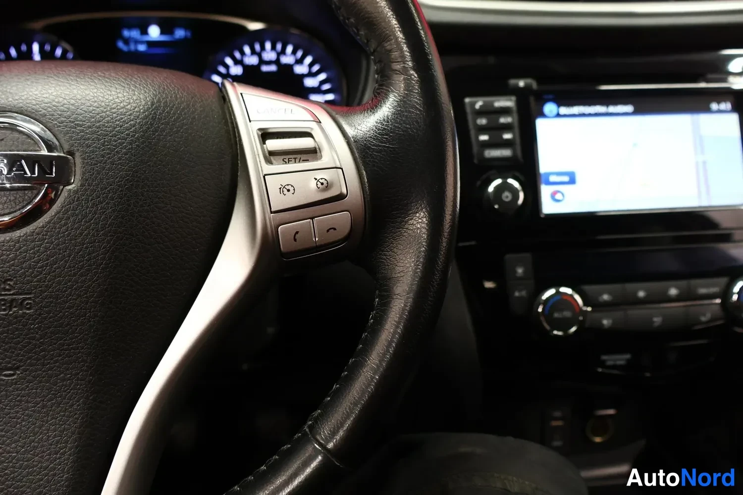 Muu: Ohjauspyörän oikea puoli ja pötköpainikkeet (SET/–, puhelin ja ääniohjaus) lähikuvassa, taustalla Nissan-merkki ja kojelaudan infonäyttö Bluetooth Audio -näkymä