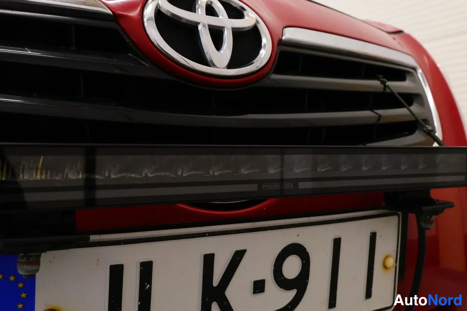 Edestä: Etusäleikkö lähikuva: Toyota-merkki, musta LED-kevytjärjestely niveltelineessä rekisterikilven yllä, kilpi K-911.