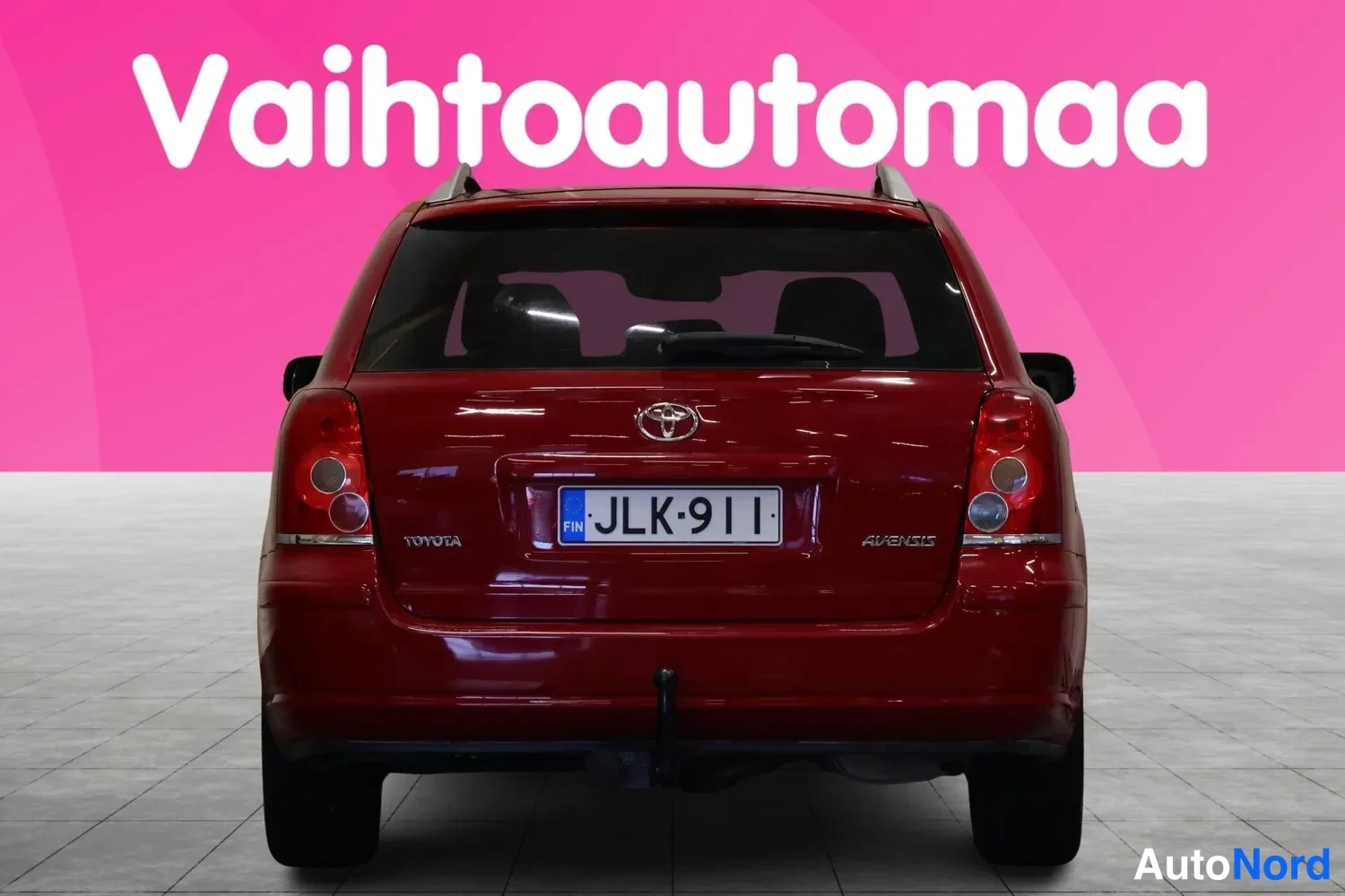 Takaa: Punaisen farmariauton takaosa suoraan takaa, Toyota-merkki, rekisterikilpi, perävaunukoukun kytkin, Avensis-teksti.