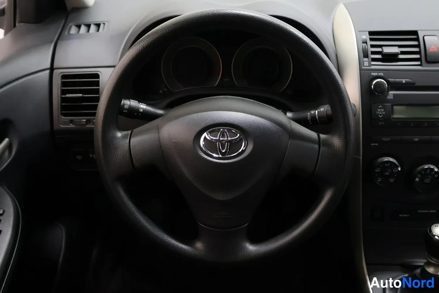 Yksityiskohta: Toyota-merkillä varustettu ohjauspyörä, kojelaudan mittaristo ja radiopaneeli näkyvät.