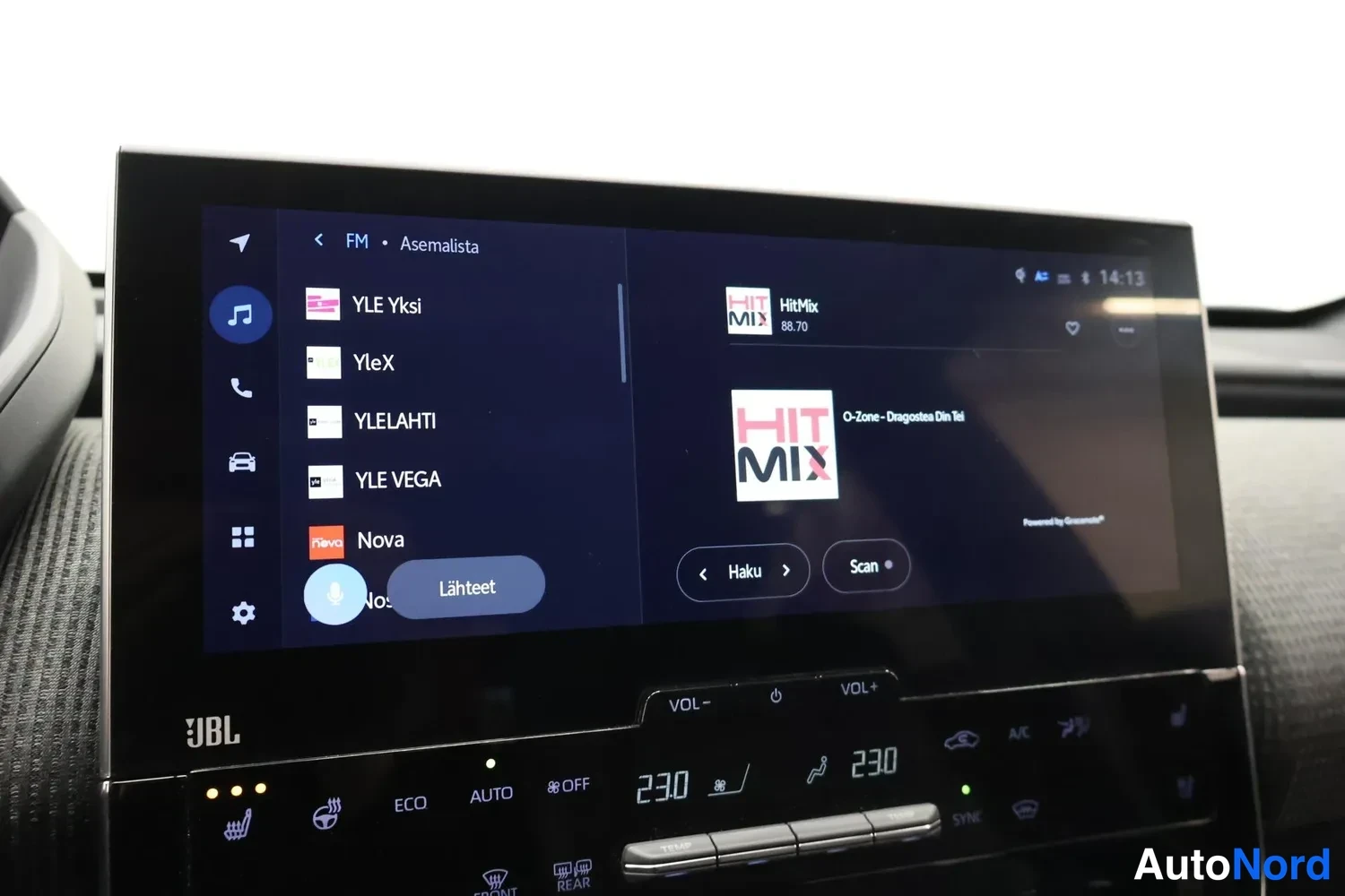 Yksityiskohta: Infotainment-näyttö auki FM-asemalistalla (YLE Yksi, YleX, YLELAHTI, YLE VEGA, Nova) JBL-merkillä ja äänenvoimakkuuspainikkeilla; lämpötilanäytöt 23,0.