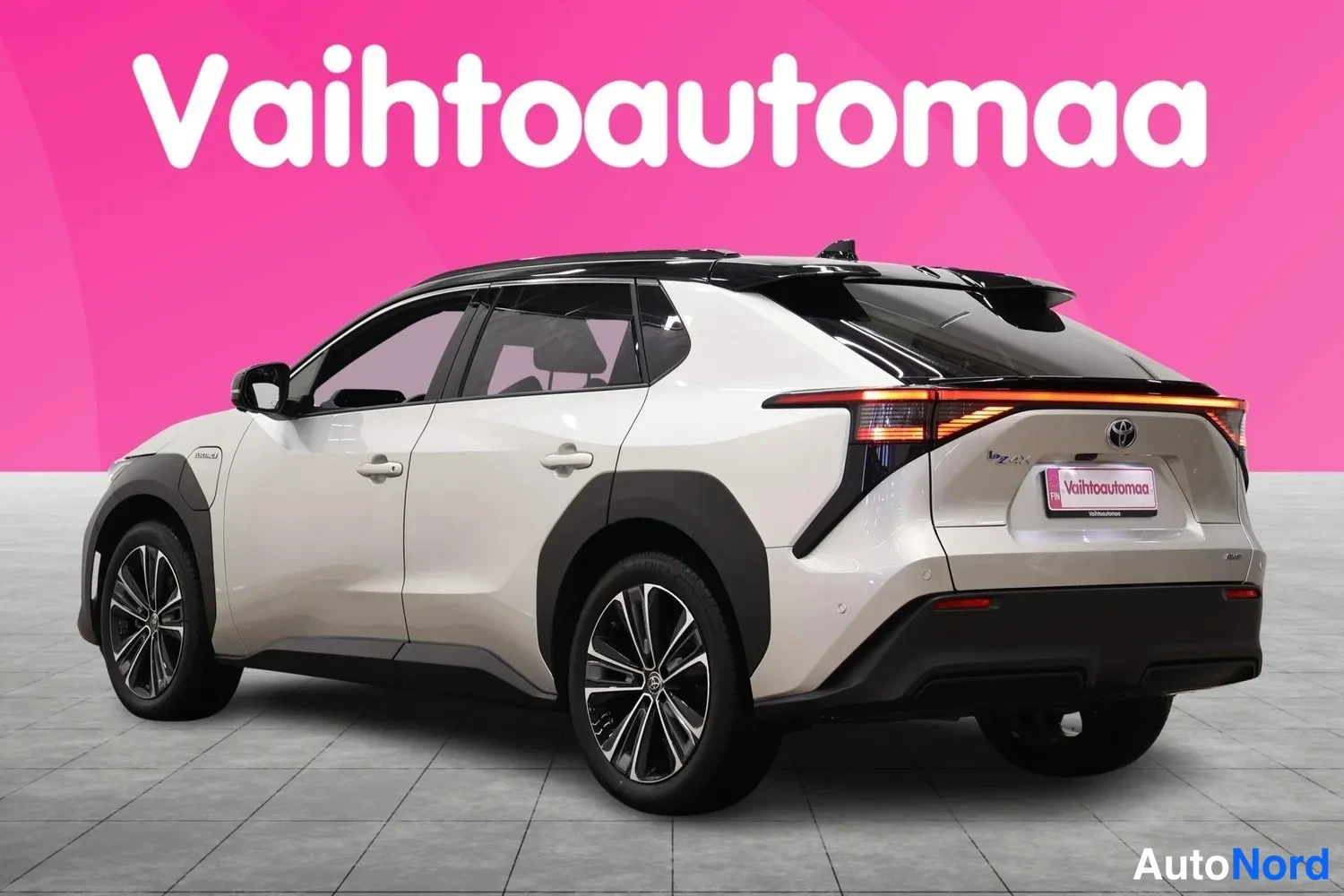 Takaviisto: Valkoisen Toyota bZ4X:n takaosakulmakuva, takavalot ja takapönttö näkyvät pinkin taustan edessä.