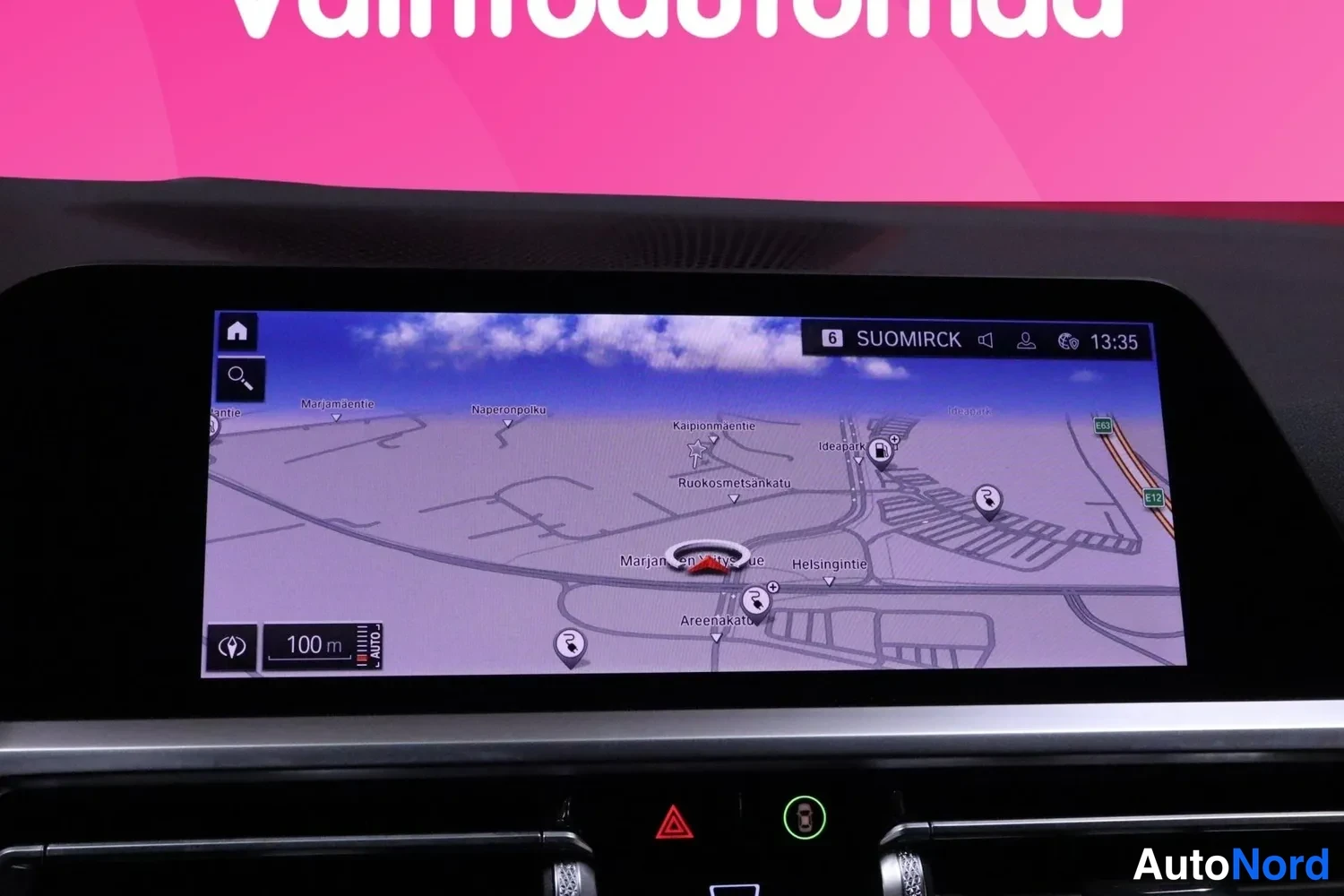 Yksityiskohta: BMW:n kojelaudan multimediatroni näyttää kartta­näkymän paikkakunnalla (mm. Ideaparkinkatu ja Marjaniementie), yläpalkissa teksti SUOMIRCK, kellon 13:35 ja etäi