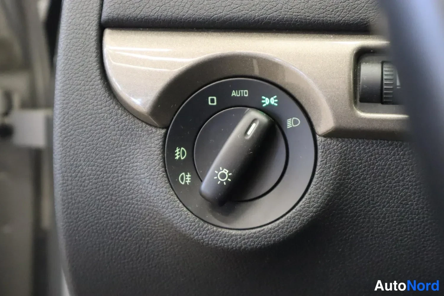 Muu: Lähikuva auton valokytkimestä kojelaudassa, jossa on AUTO-asento ja lukuisia valaistussymboleita.