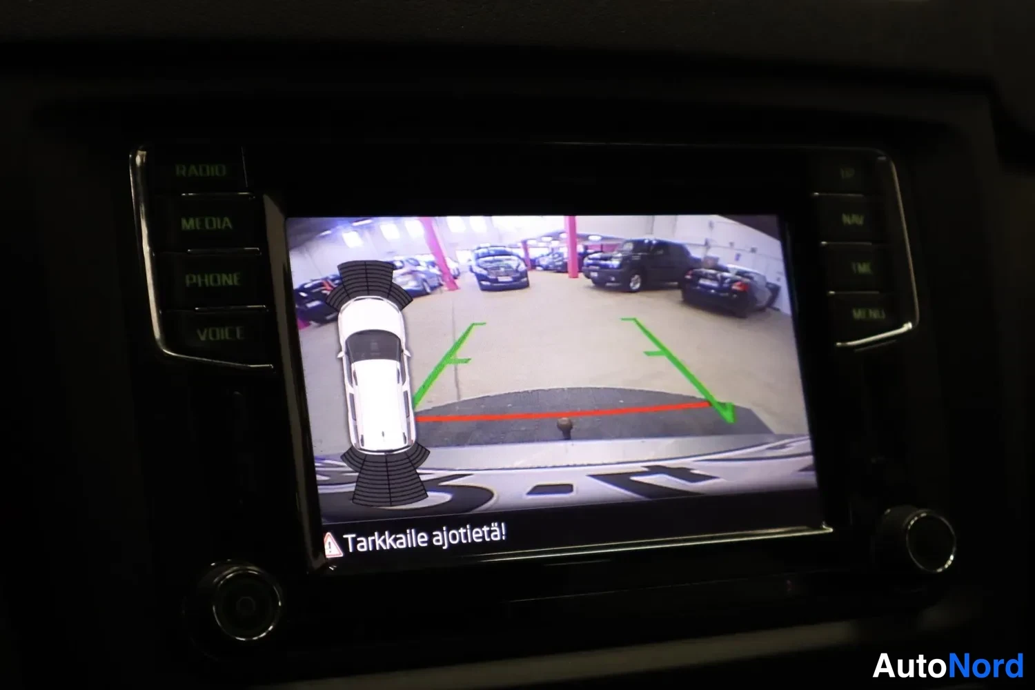 Muu: Infotainment-näytöllä peruutuskameran kuva parkkihallista ja kaariviivat, teksti 'Tarkkaile ajotietä!'.