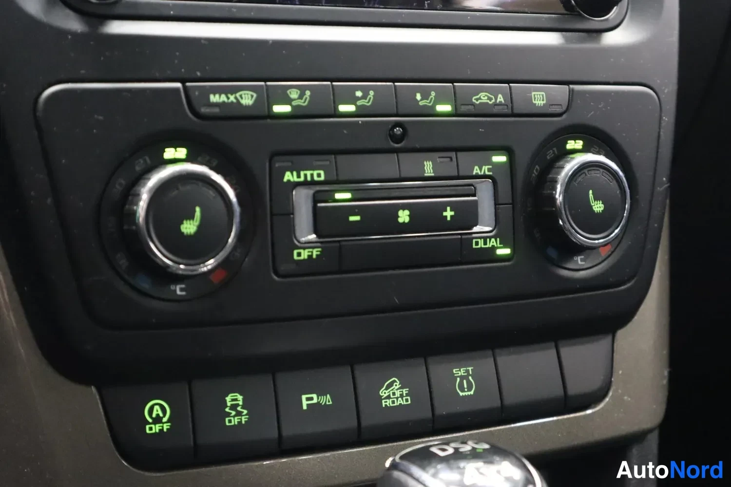 Yksityiskohta: Lähikuva auton ilmastointipaneelista: kaksi säädinkiekkoa näytöillä 22, AUTO-, A/C-, OFF- ja DUAL-toiminnot, ylärivissä lämmityspainikkeet ja alarivissä painikk