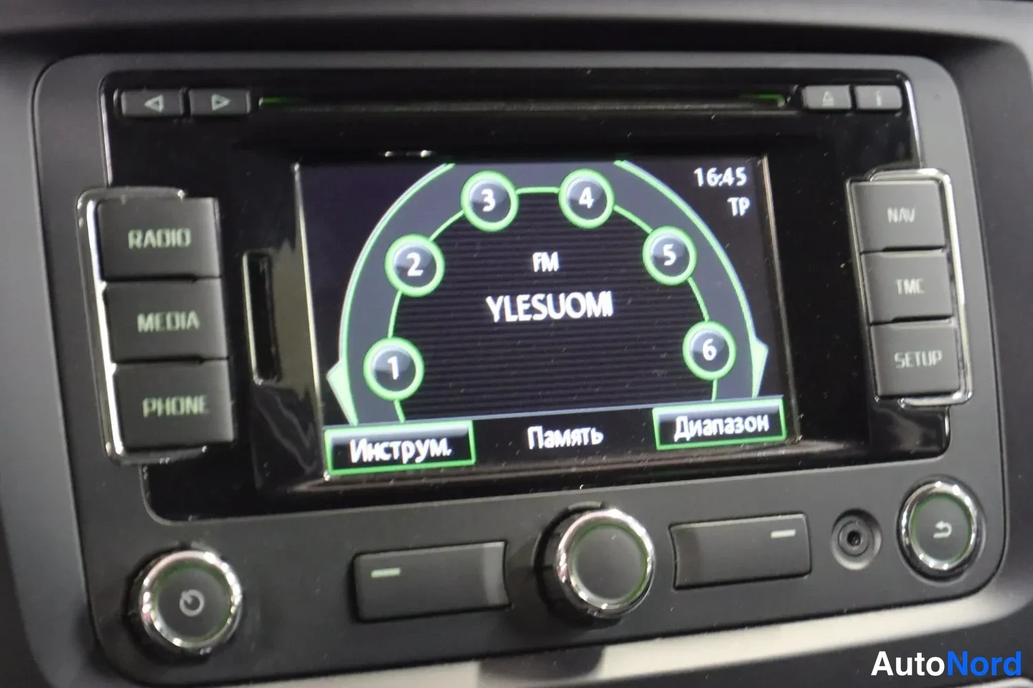 Yksityiskohta: Keskiohjaimen radio näyttö RU-osiossa: näytöllä FM YLESUOMI ja numeeriset esiasetukset 1–6, aikana 16:45 ja TP-merkinnät; sivupainikkeet RADIO, MEDIA, PHONE, NA