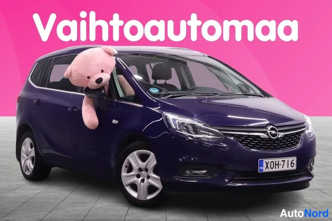 Etuviisto, nokka oikealle: Tummansininen tila-auto kolmivaiheisessa etunurkkakuvassa oikealle suunnattuna, rekisterikilpi, näyttävästi valaistussa studiotaomaisessa tilassa vaalean
