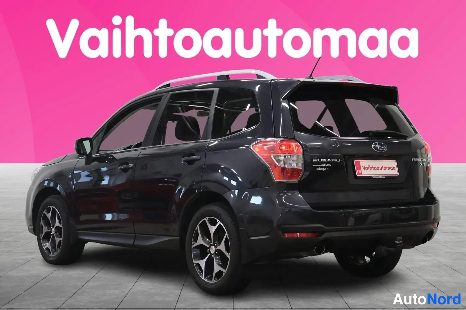 Takaviisto: Tummanharmaa Subaru Forester takkulmasta vasemmalta, takaluukissa XT-tunnuksissa ja katolla kattokaiteet.
