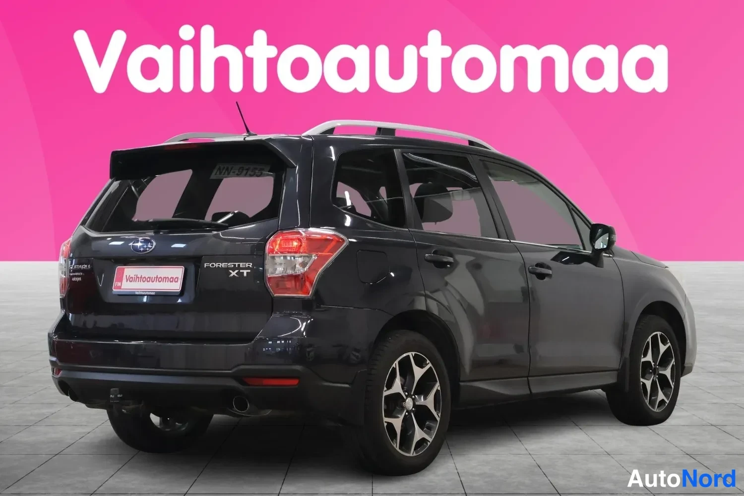 Takaviisto: Subaru Forester XT takaapäin viistosti: tummansininen kori, FORESTER XT-merkintä, kattokaiteet, hopeavanteet ja vetokoukku näkyvät.