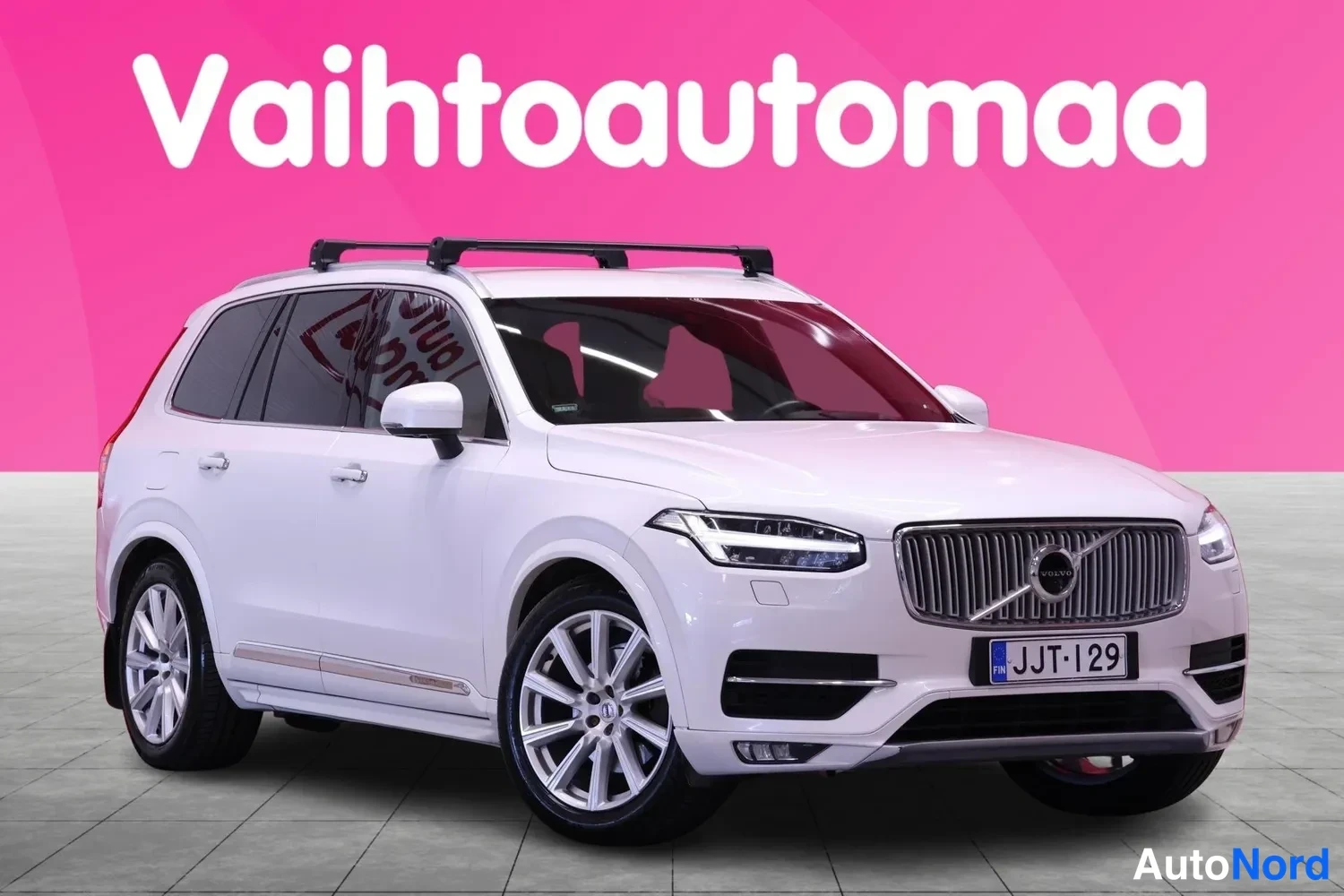 Etuviisto, nokka oikealle: Valkoinen Volvo XC90 etuviistosta, keula kuvan oikealla laidalla. Kattotelineet ja rekisteritunnus näkyvissä.
