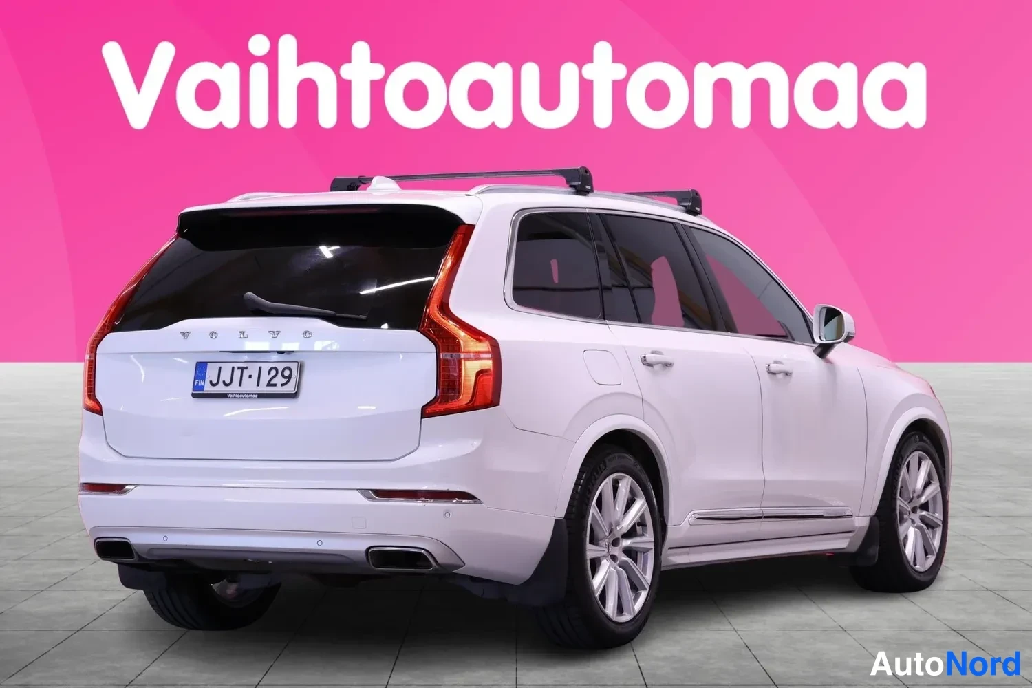 Takaviisto: Valkoinen Volvo XC90 takaviistosta, perä vasemmalla. Peräluukussa VOLVO-teksti, rekisteritunnus ja kattotelineet näkyvissä.