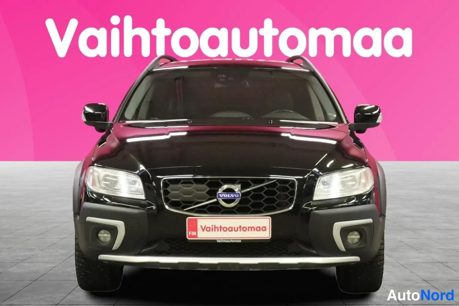 Edestä: Musta farmariauto suoraan edestä kuvattuna; VOLVO-merkki etusäleikössä, ajovalot, sumuvalot ja etupuskurin kromilista näkyvät.