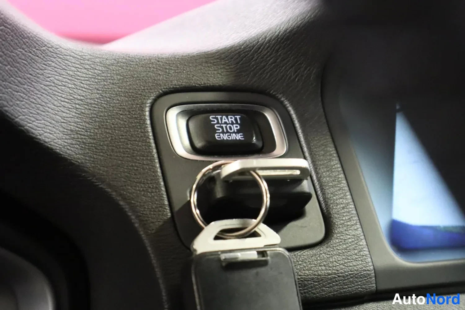Muu: Start/Stop Engine -käynnistyspainike kojelaudassa, avainkaksoisrenkaassa ripustettu avain kuva edessä.