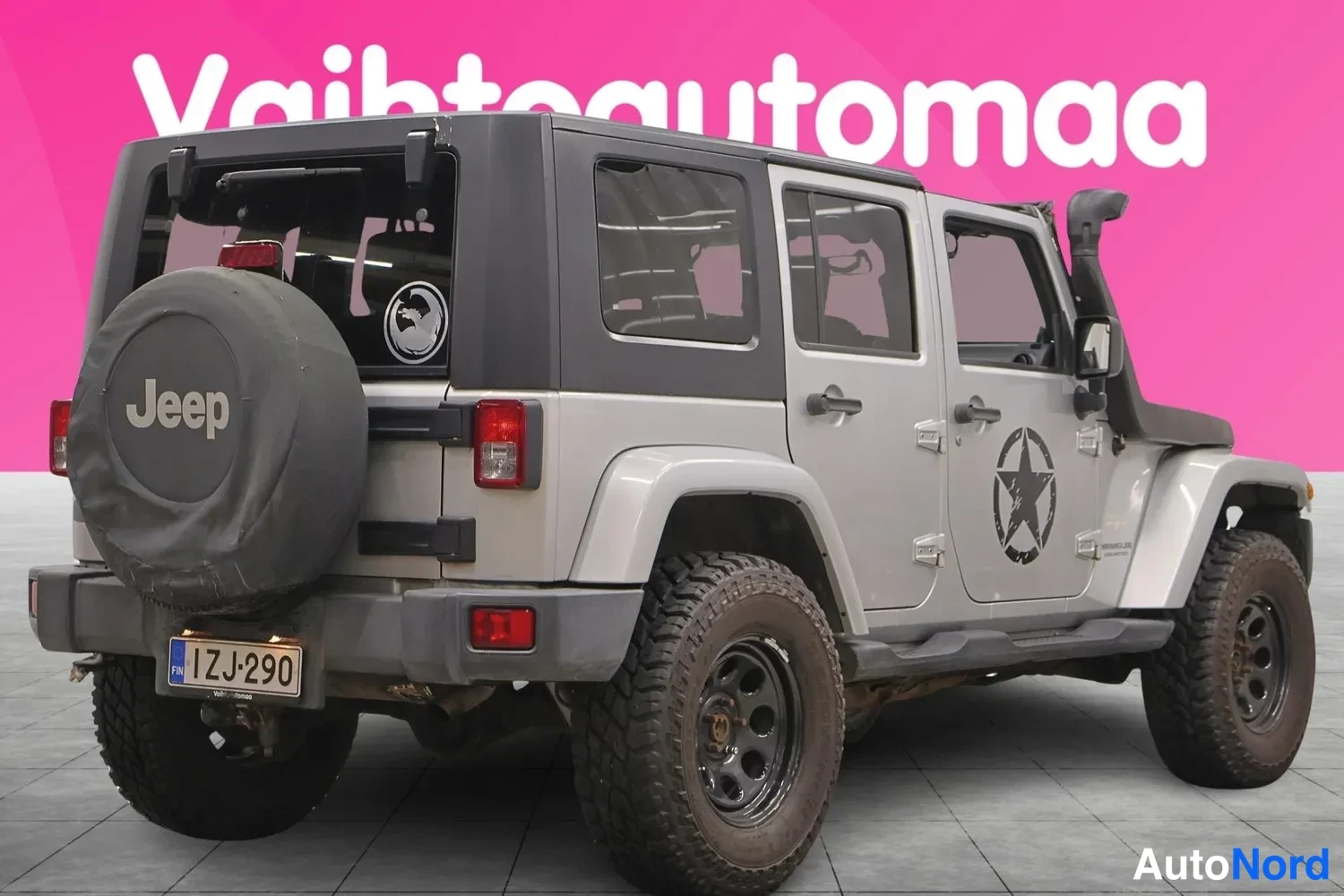 Takaviisto: Hopeanharmaa Jeep Wrangler oikealta takakulmalta kuvattuna; Jeep-tekstillä varustettu varalippu, rekisteritunnus, tumma kova katto ja neljä ovea näkyvissä.