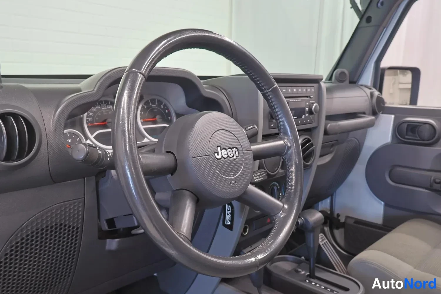 Muu: Ohjaamon sisäkuva: Jeep-merkkinen ohjauspyörä, mittaristo, radio-CD-yksikkö kojelaudassa ja automaattivaihteen valitsin keskikonsolissa.